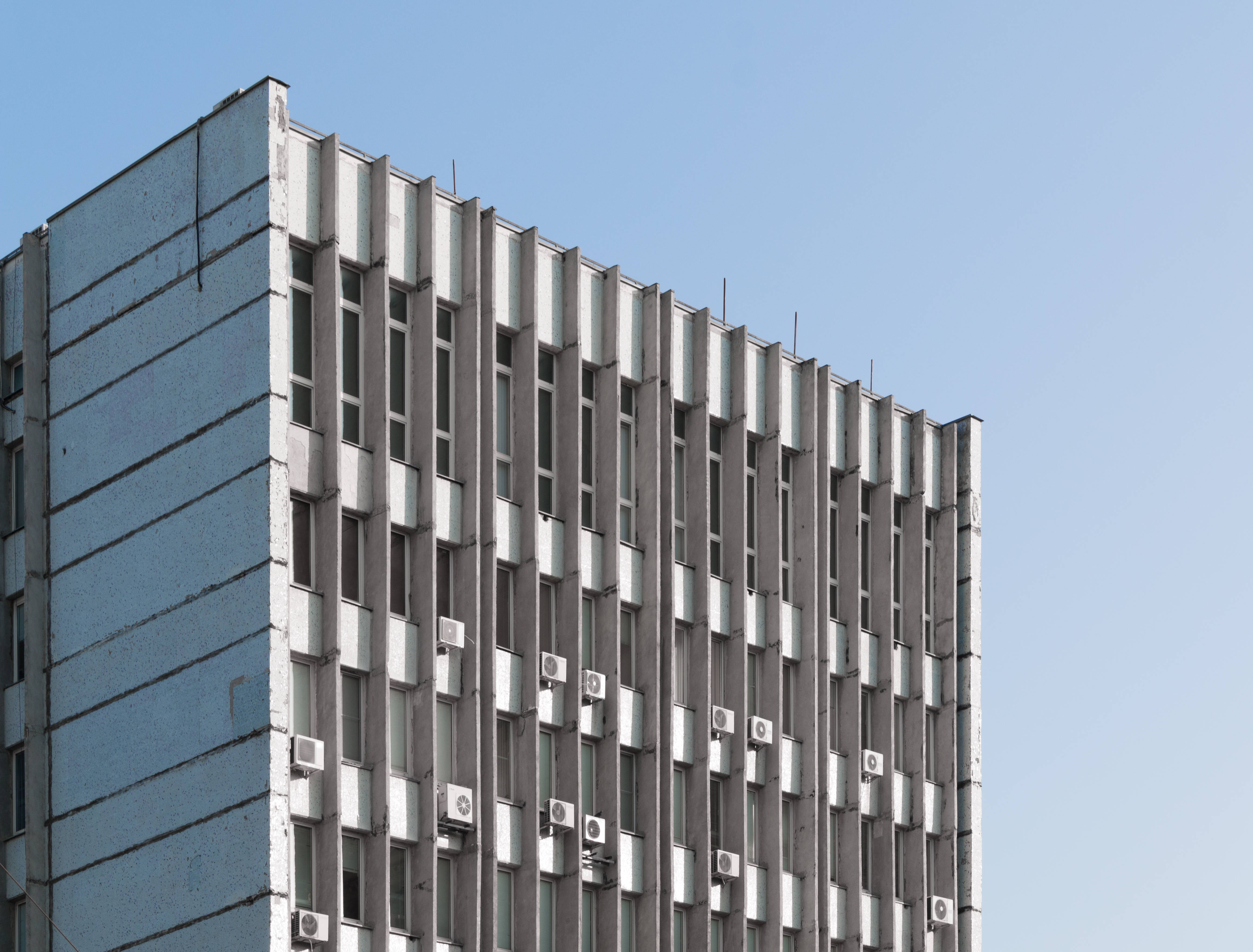 摩爾多瓦基希納烏蘇聯建築 壁紙 — 一座鮮明的現代主義建築，帶有重複的垂直窗戶和空調機，矗立在清澈的藍天下。