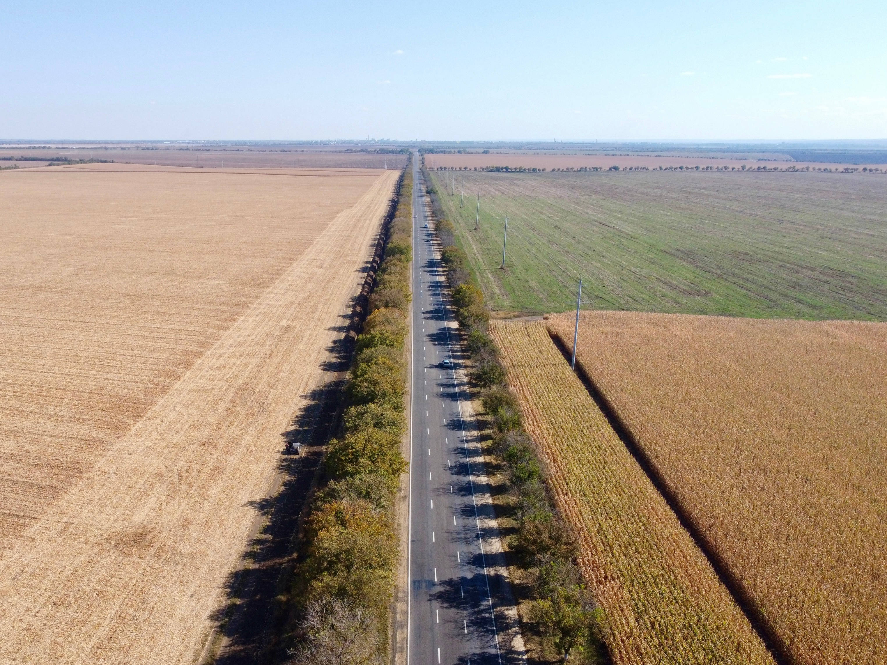 摩爾多瓦基希納烏鄉間小路 壁紙 — 晴朗藍天下，一條筆直道路兩旁是金色和綠色的農田的鳥瞰圖。