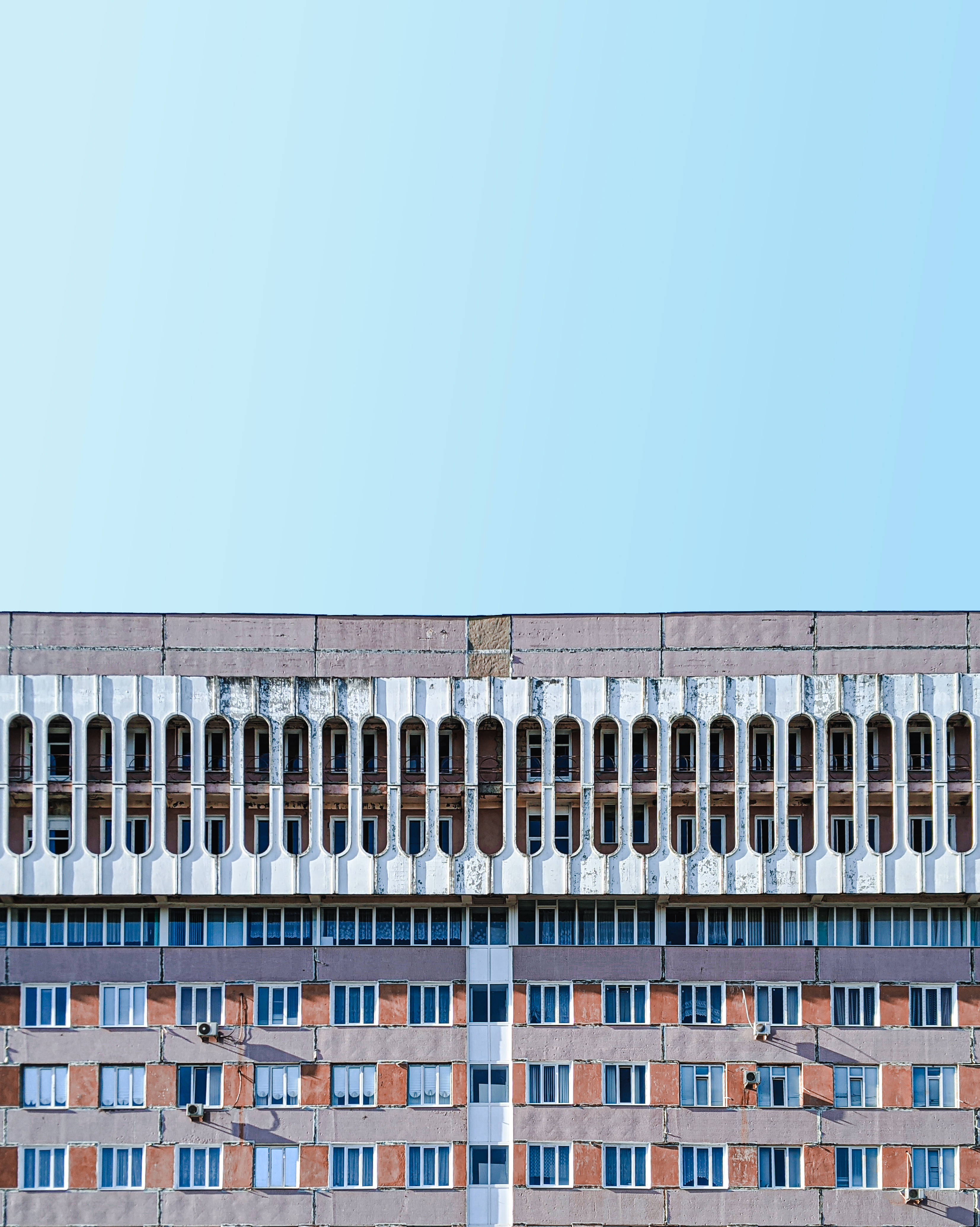 摩爾多瓦癌症研究所建築 壁紙 — 一座風化的粗獷主義公寓大樓，帶有重複的拱形窗戶，矗立在清澈的淡藍色天空下。