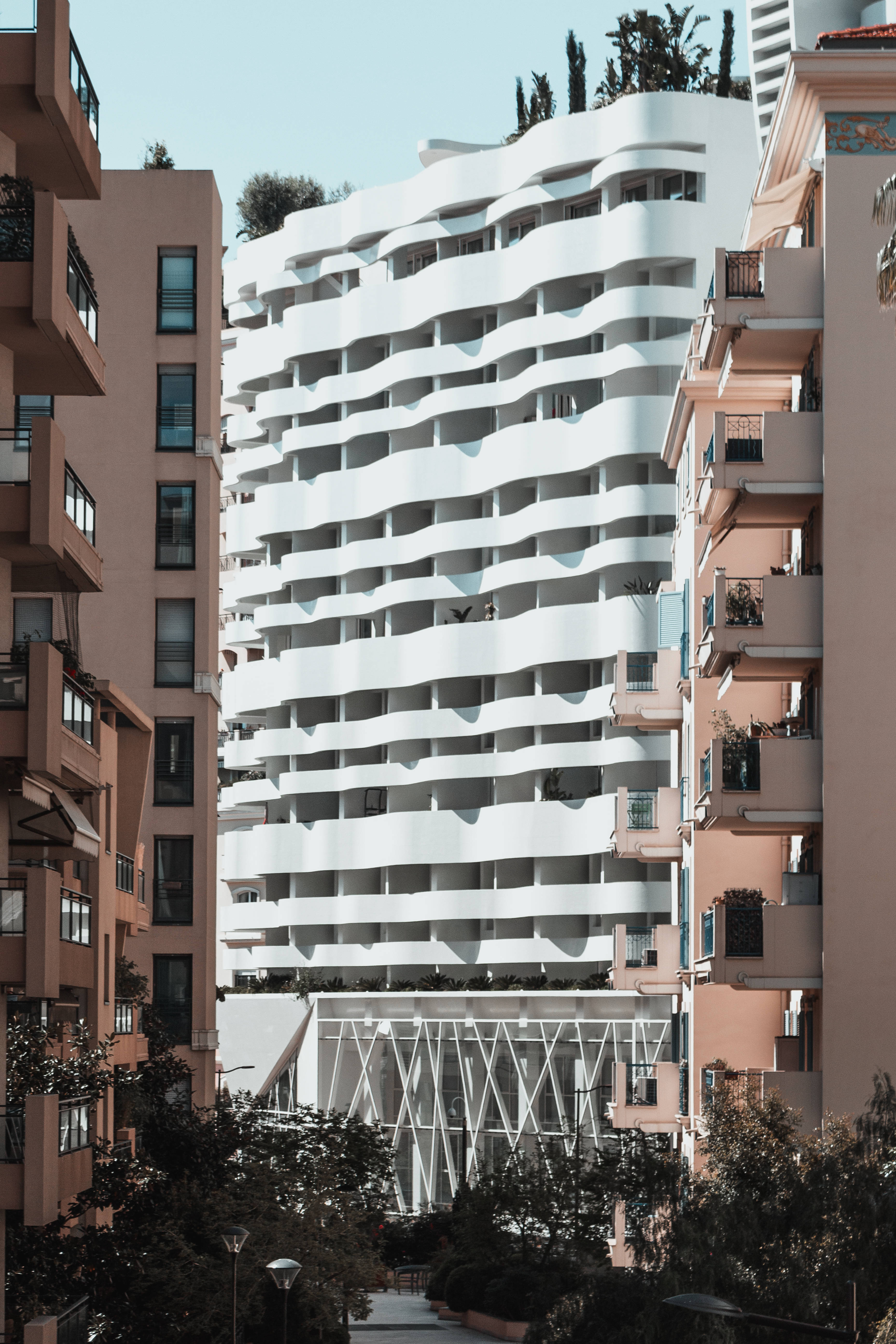 摩納哥白色建築 壁紙 — 一座引人注目的白色波浪形現代建築矗立在陶土色公寓樓之間，在清澈的藍天下。