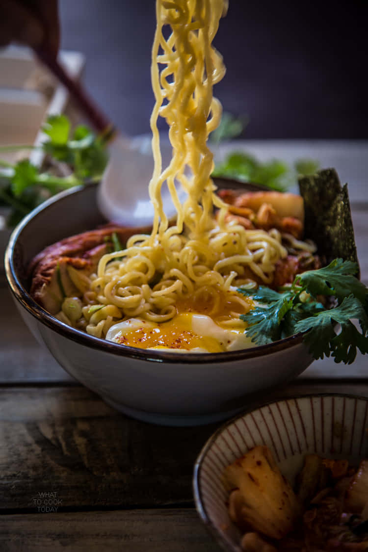 撈麵麵條特寫 壁紙 — 一碗冒煙的拉麵，筷子夾起麵條，露出流心蛋和新鮮芫荽。