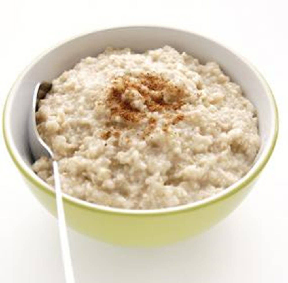 撒上肉桂粉的燕麥粥 壁紙 — 一碗 creamy 燕麥片，上面撒了肉桂粉，放在淺綠色陶瓷碗裡，裡面有湯匙。