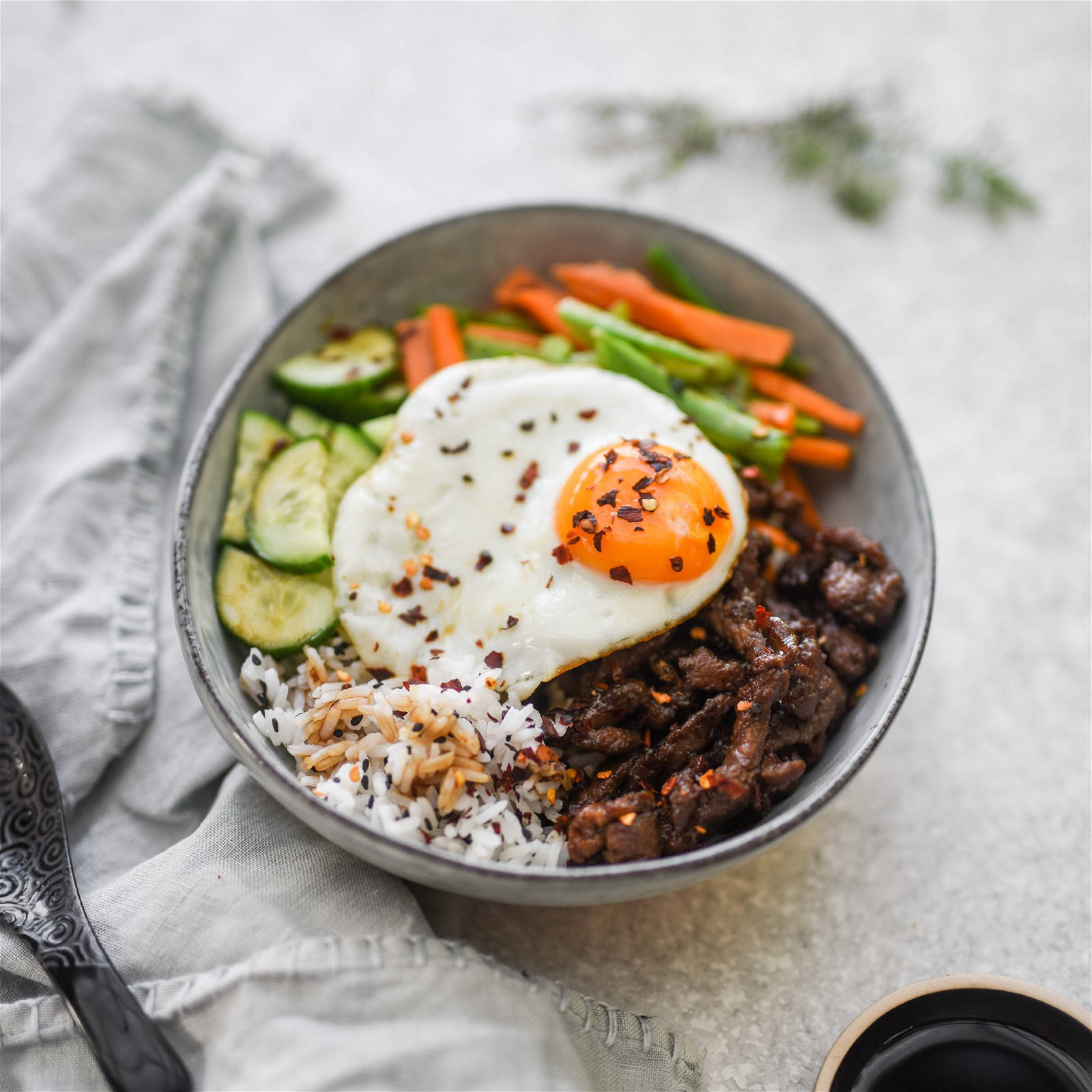 撒上黑芝麻的拌飯 壁紙 — 一碗色彩繽紛的米飯、牛肉和蔬菜，上面放著太陽蛋和紅辣椒片。