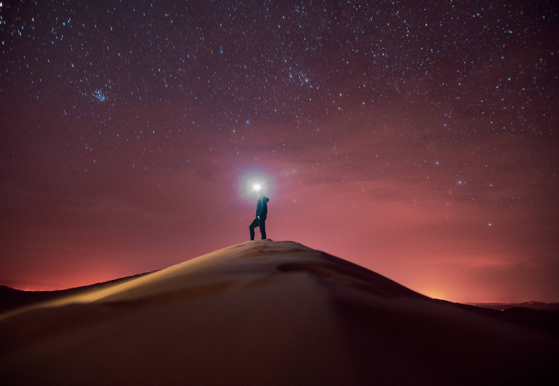 夜晚站在沙丘上，頭燈在星空下閃耀的人。
