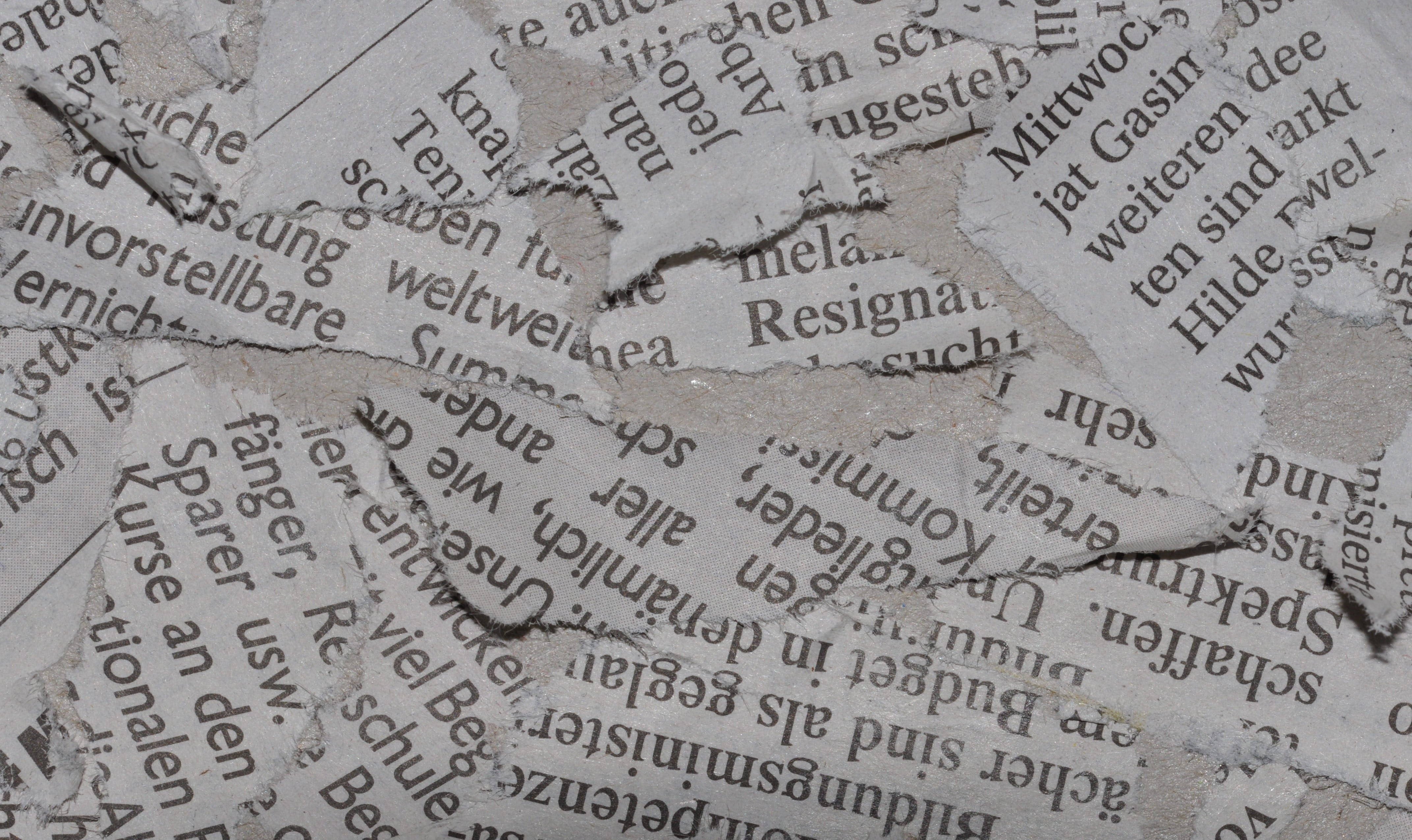 Newspaper 桌布 壁紙 — 撕碎報紙碎片的特寫，在紋理灰色背景上顯露出零碎的德文文字。