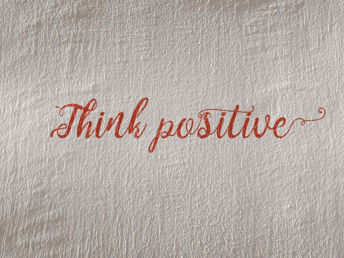 紅色閃粉草書文字寫在帶紋理的銀色牆上，內容為「Think positive」