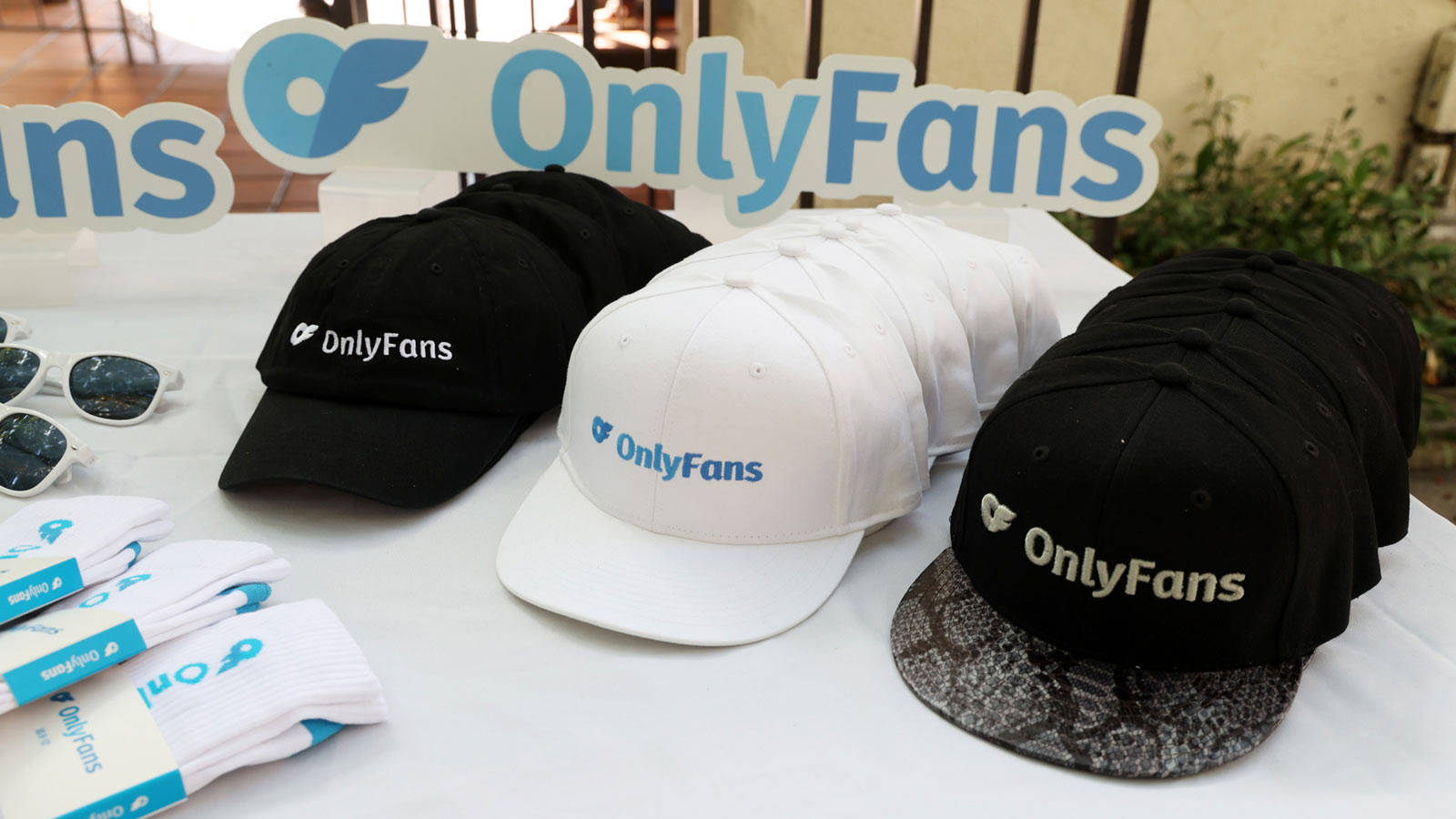 擁抱你的風格：OnlyFans 品牌商品 壁紙 — 展示OnlyFans品牌商品，包括黑白帽子和襪子，擺放在白色桌子上，背景有一個大型OnlyFans標誌。