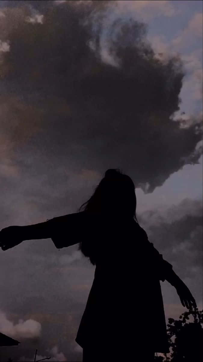 一個人在戲劇性的多雲暮色天空下張開雙臂的剪影。