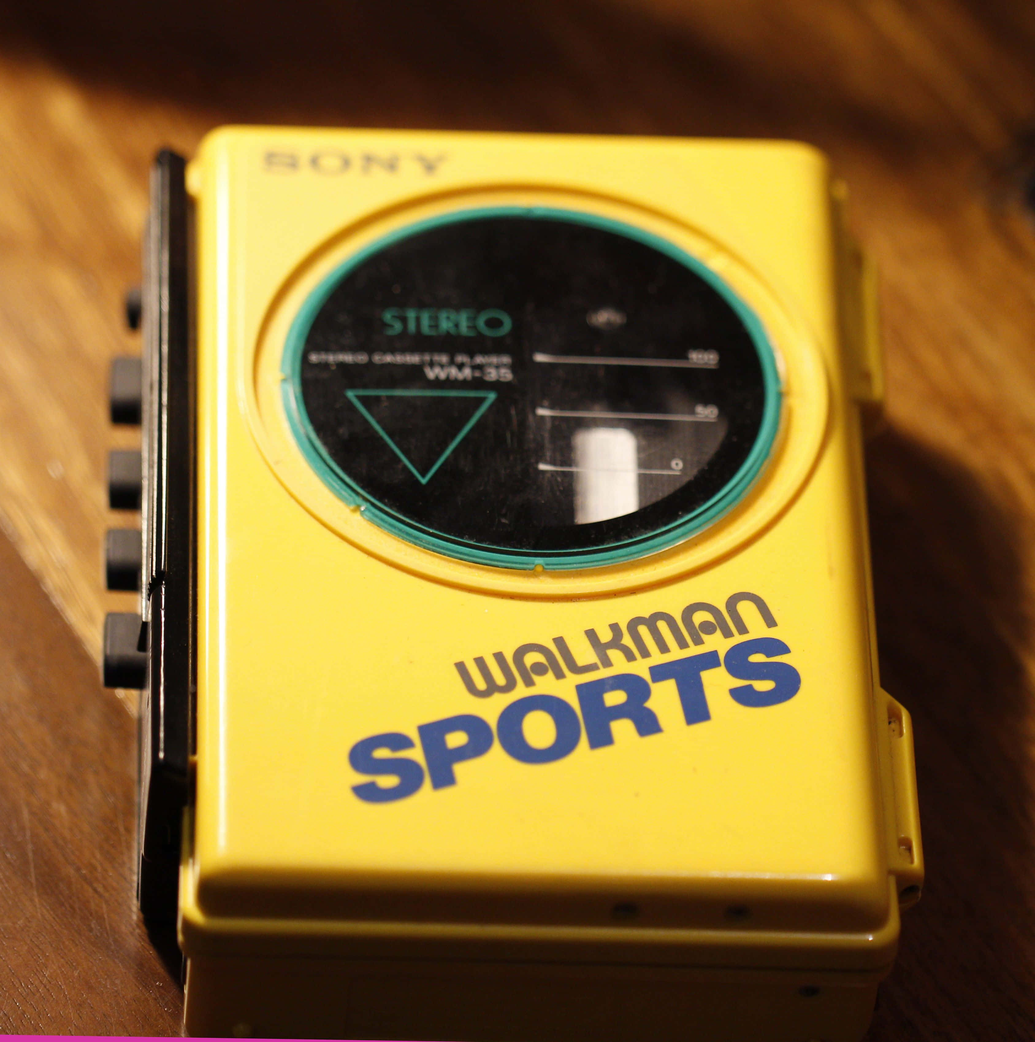 擁抱八十年代的懷舊回憶 壁紙 — 一部復古黃色Sony Walkman Sports WM-35卡式錄音機放在木質表面上，在溫暖燈光下。