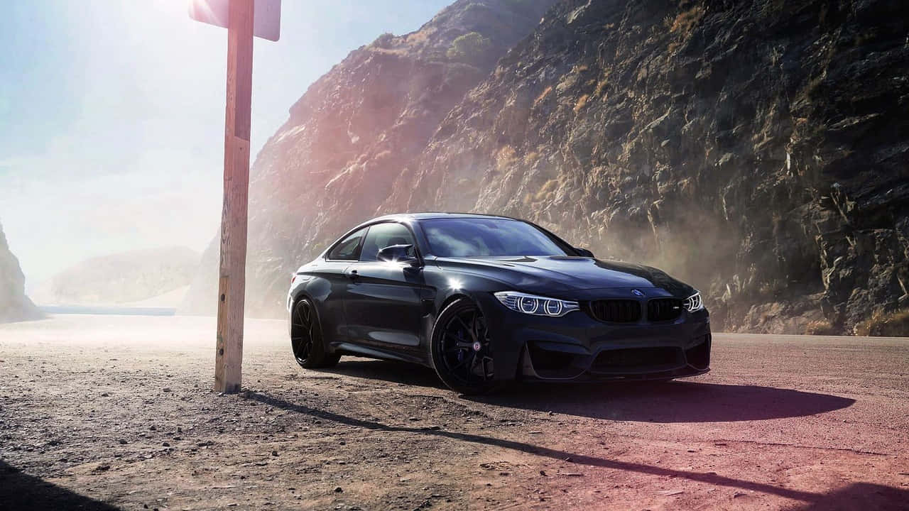 擁抱奢華，駕馭BMW 壁紙 — 一輛時尚的黑色BMW M4雙門跑車停泊在塵土飛揚的路邊，背後是崎嶇的懸崖峭壁，在明亮的陽光下。