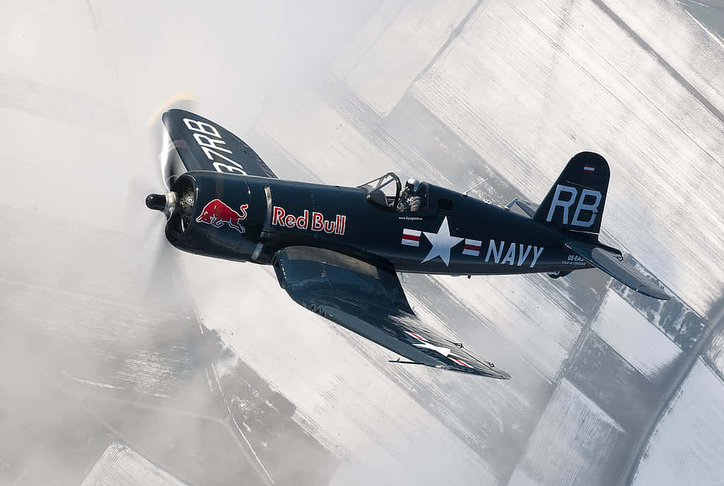 帶有 Red Bull 標誌的復古海軍戰鬥機在雪地跑道上低空飛行。