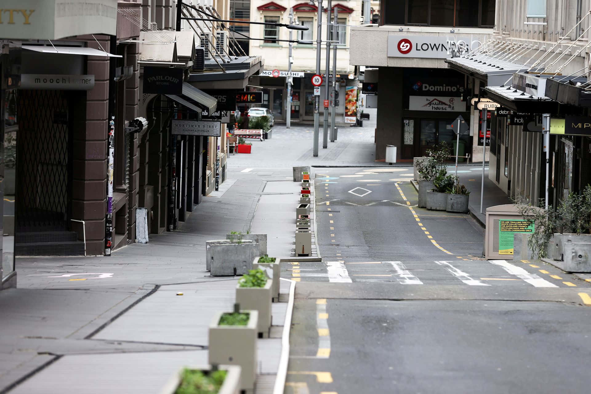擁抱灰色之美 壁紙 — 一條空蕩蕩的城市街道，兩旁是關閉的商店和混凝土花盆，在陰天的日光下。