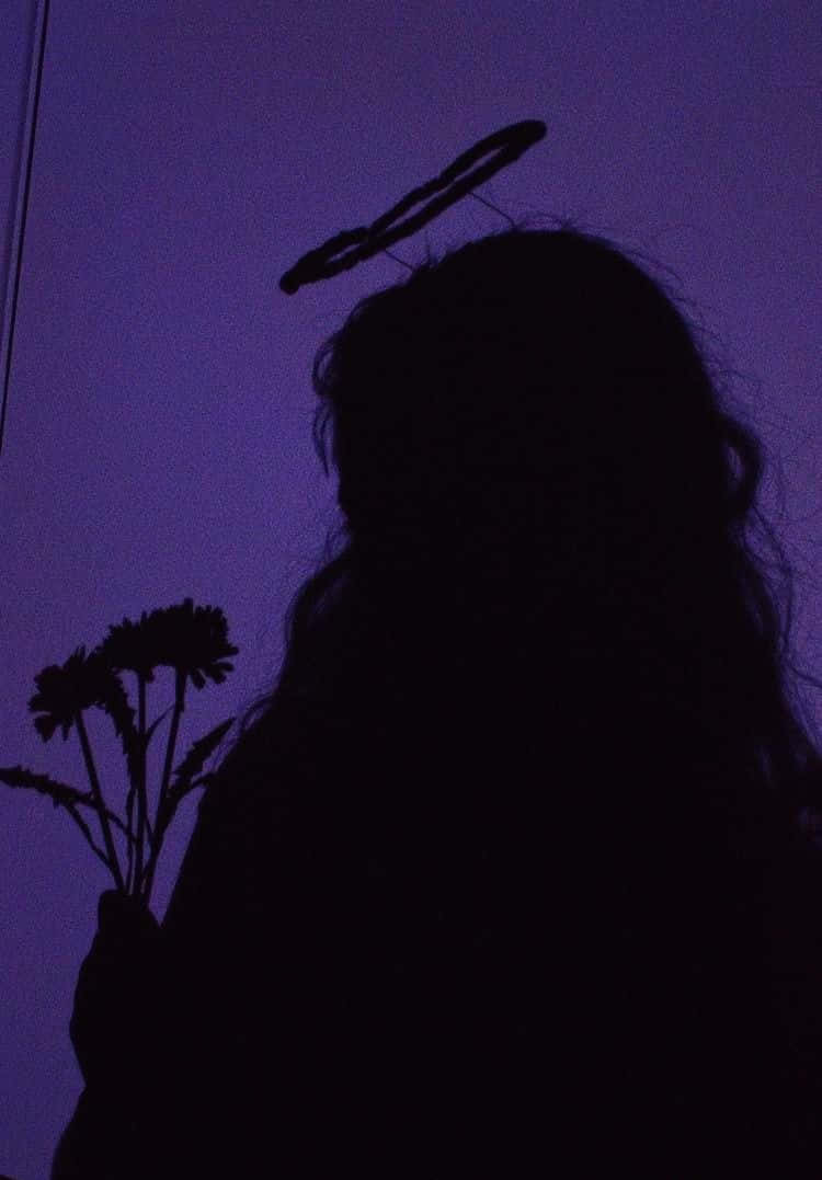 擁抱紫調美學的浪漫魅力 壁紙 — 一個帶有光環的人手持鮮花，背景是深紫色的暮色天空的剪影。