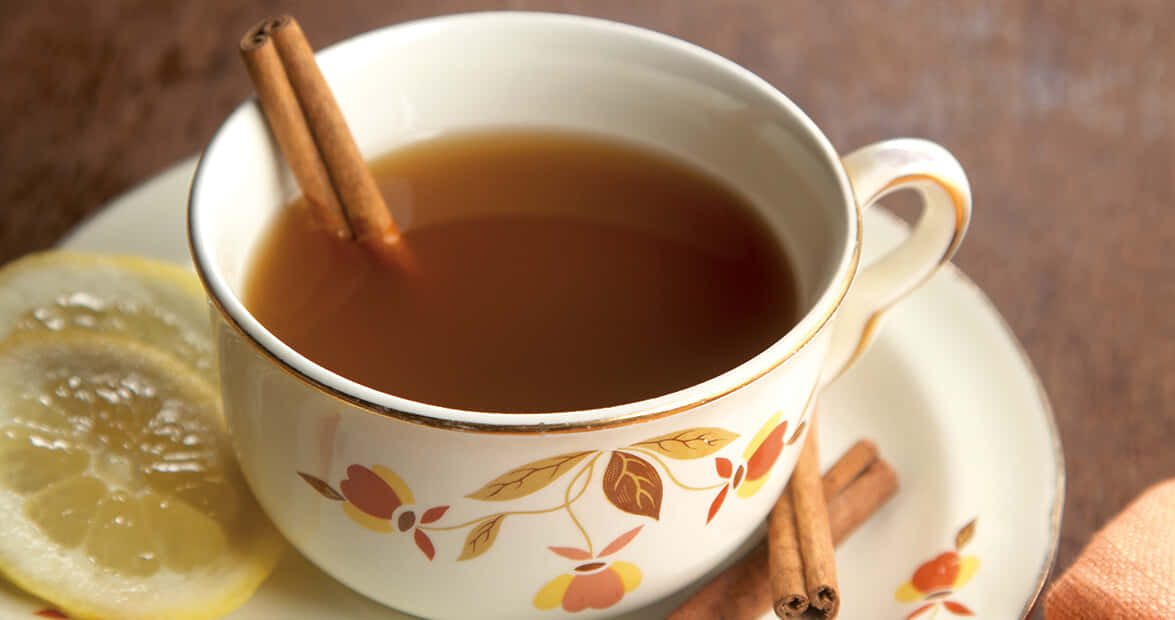 擁抱自然，靜享晨茶 壁紙 — 一杯冒煙的香料茶，配以肉桂棒和檸檬片，放在花卉圖案的碟子上。