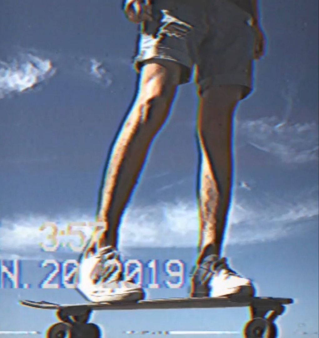擁抱自由：復古滑手對藍天 壁紙 — 一個人企喺滑板上，背景係帶有故障效果嘅藍天白雲同數碼疊加文字。