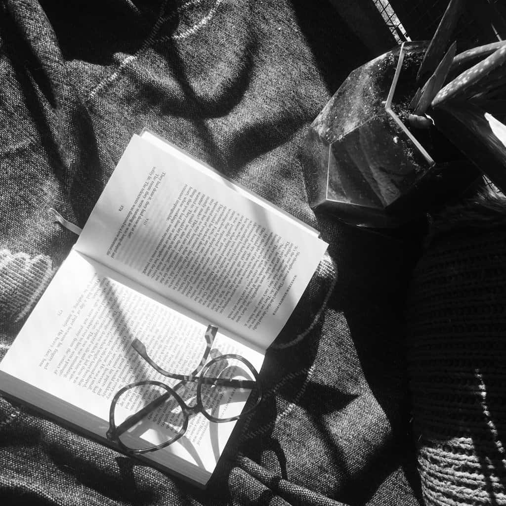 黑白布料上打開的書本、眼鏡和植物。