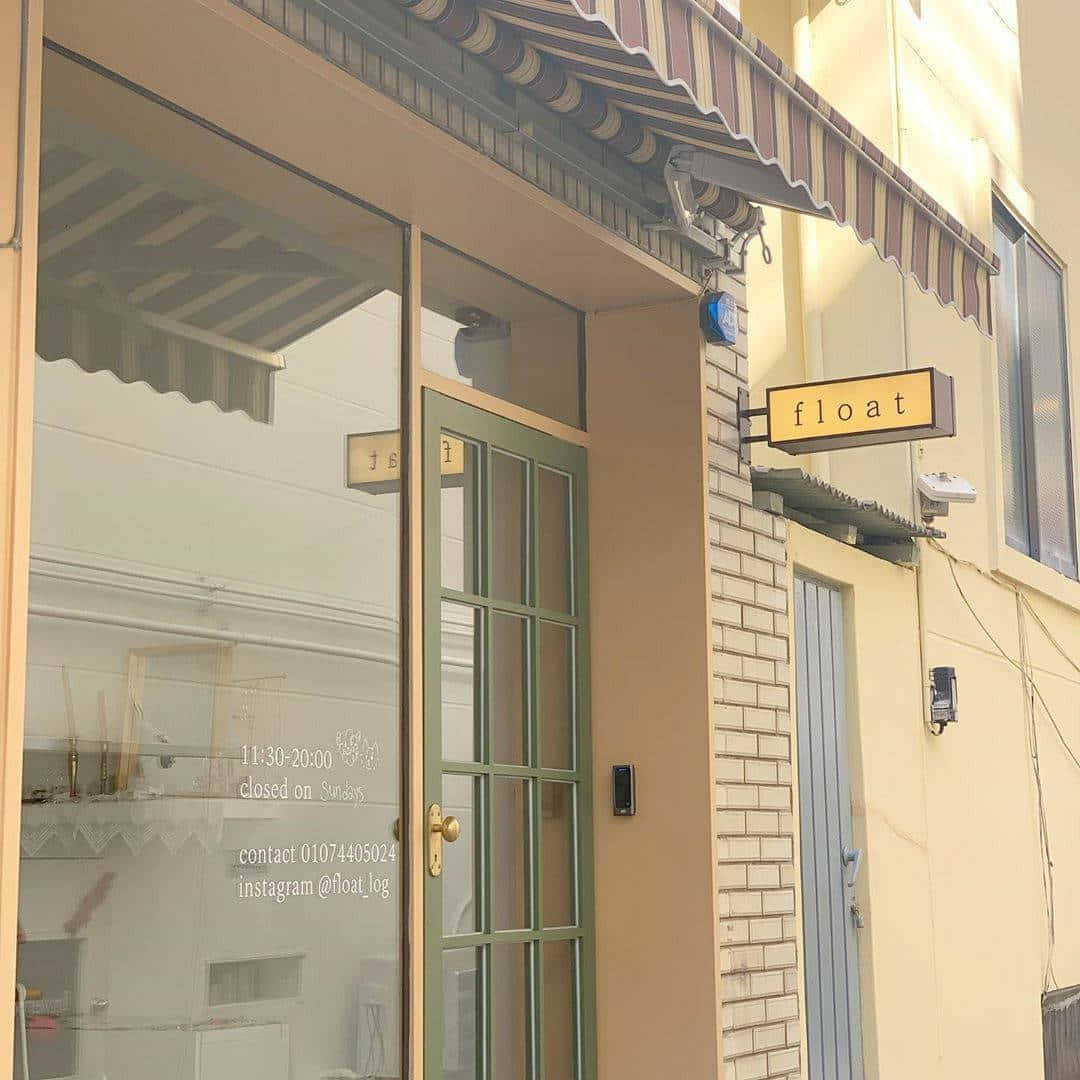 擁抱雅緻米色的美 壁紙 — 陽光普照的店舖門面，帶有條紋遮陽篷和玻璃門，反射街道，黃色招牌上寫著 float。