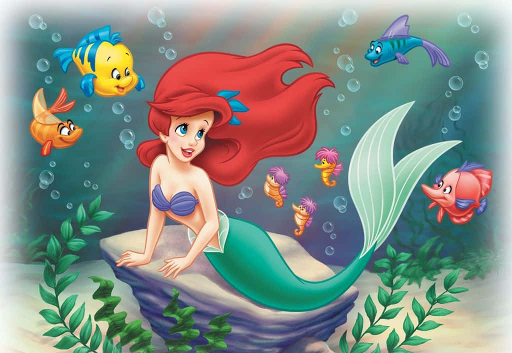 小美人魚 桌布 壁紙 — 擁有飄逸紅髮的美人魚愛麗兒坐在岩石上，周圍是色彩繽紛的魚和氣泡，構成一個海底場景。