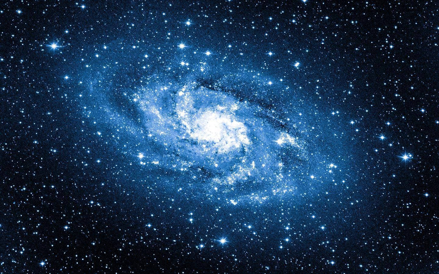 擴張藍色星系 壁紙 — 一個令人驚嘆的螺旋星系，在佈滿星星的宇宙背景下發出藍色和白色的光芒。