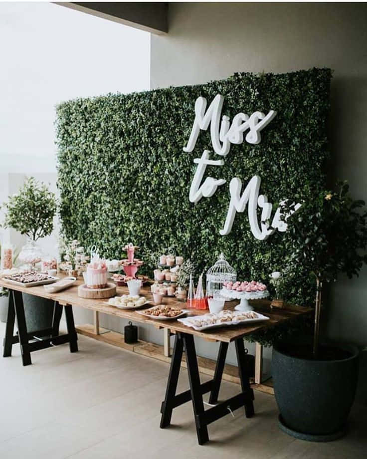 婚禮甜品桌，粉紅色美食襯托綠色樹籬牆，附有「Miss to Mrs」標牌。
