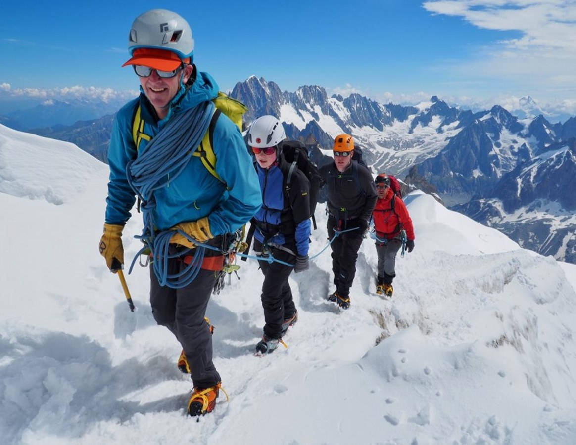 四名登山者正在攀登白雪覆蓋的山脊，身後是積雪的山峰。