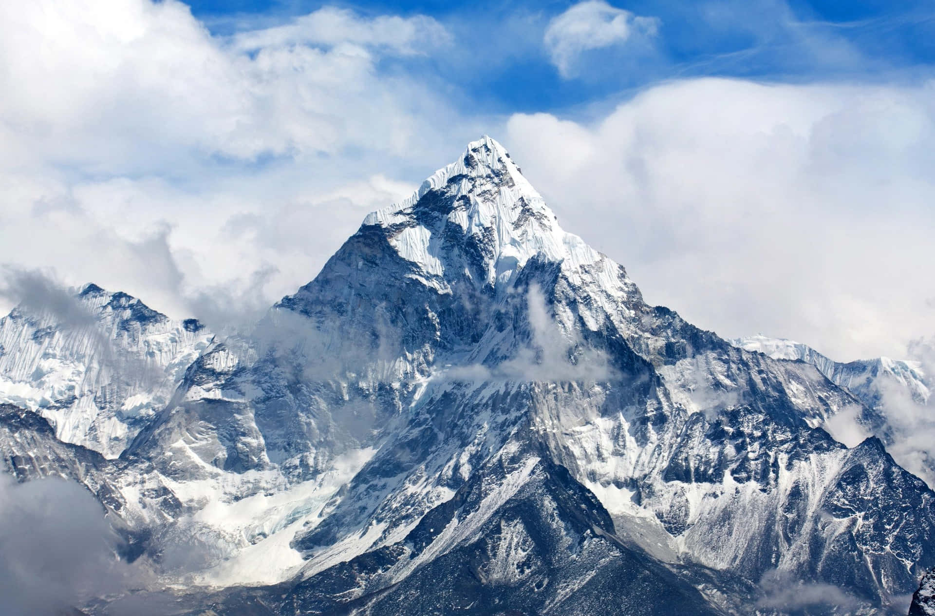 雪山峰頂高聳於雲層之上，藍天為背景