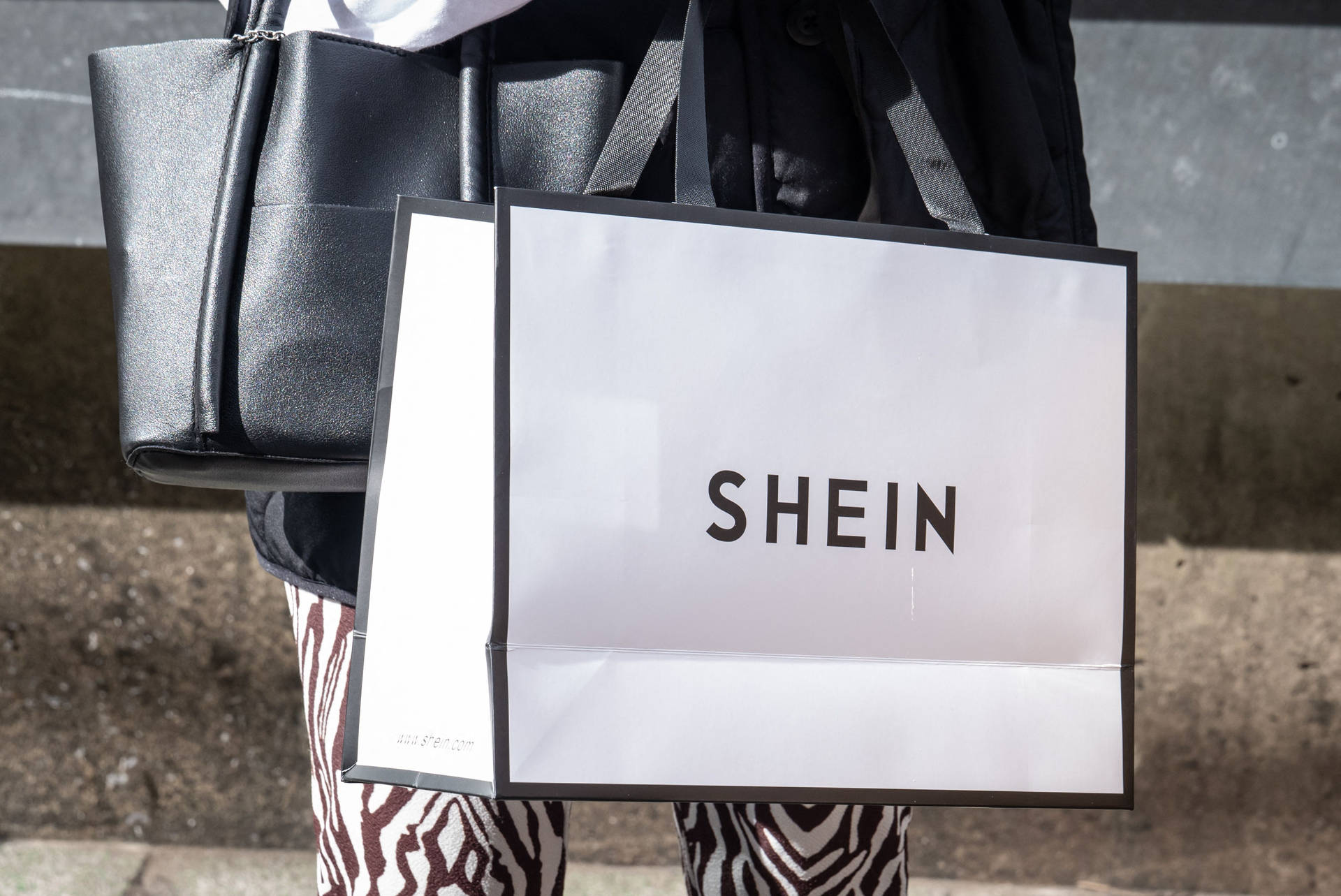 人在混凝土階梯上拿著Shein購物袋和黑色手提袋。