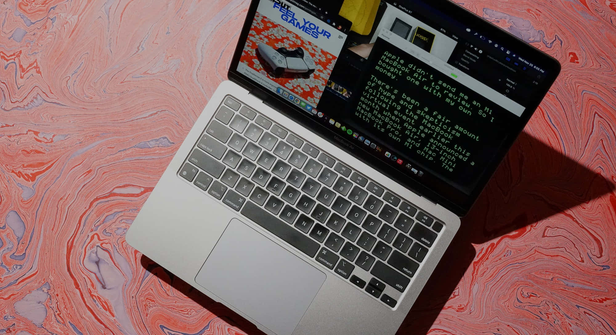 攜帶MacBook，輕鬆度過每一天 壁紙 — 銀色手提電腦打開在旋轉的粉紅色和紫色大理石表面上，顯示遊戲內容和文字。