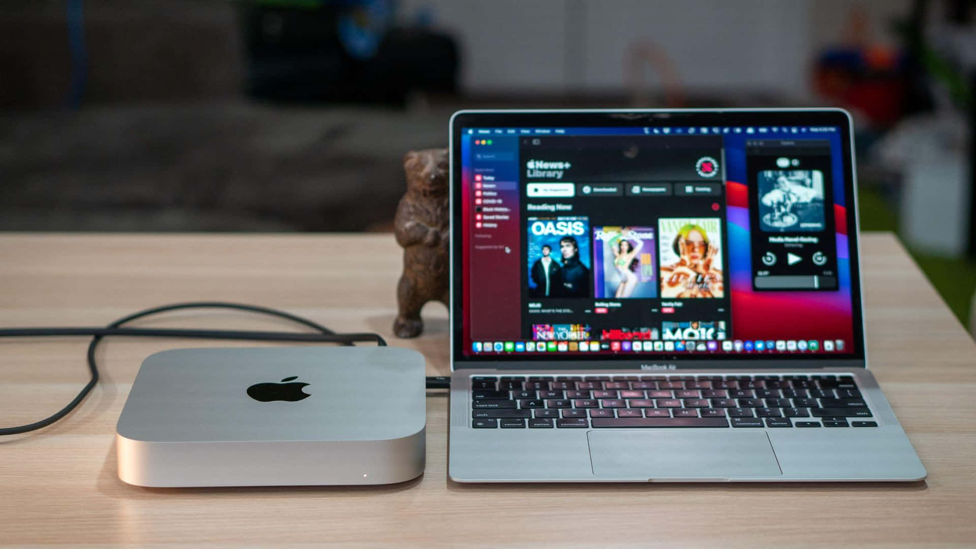 攜帶MacBook隨時工作 壁紙 — 一部銀色 Mac mini 和 MacBook Pro 並排放置在木桌上，附近有一個小熊公仔。