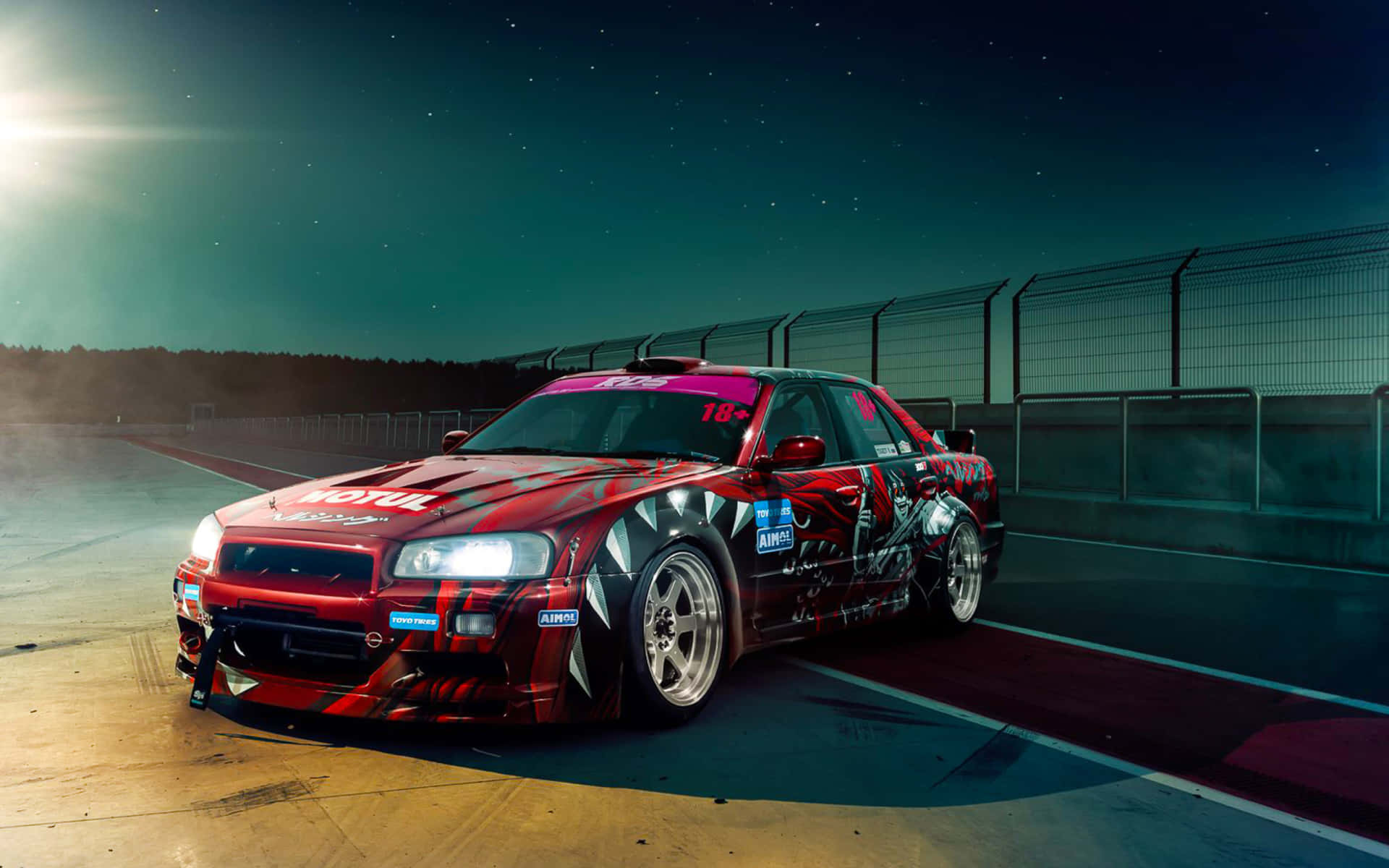 改裝 Nissan Skyline R33 GTR 壁紙 — 一輛帶有黑色火焰貼紙的紅色飄移車在星空下夜間賽道上奔馳，車頭燈閃閃發光。
