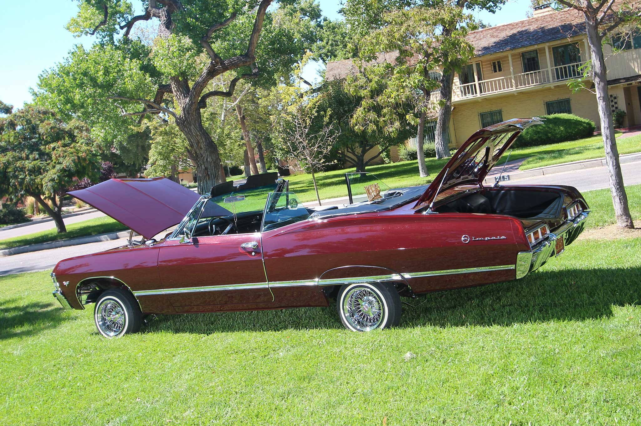 改裝雪佛蘭Impala 1967 壁紙 — 一架經典栗色開篷車，引擎蓋和後備箱打開，停放在陽光普照的綠色草坪上，旁邊是一間黃色房子。