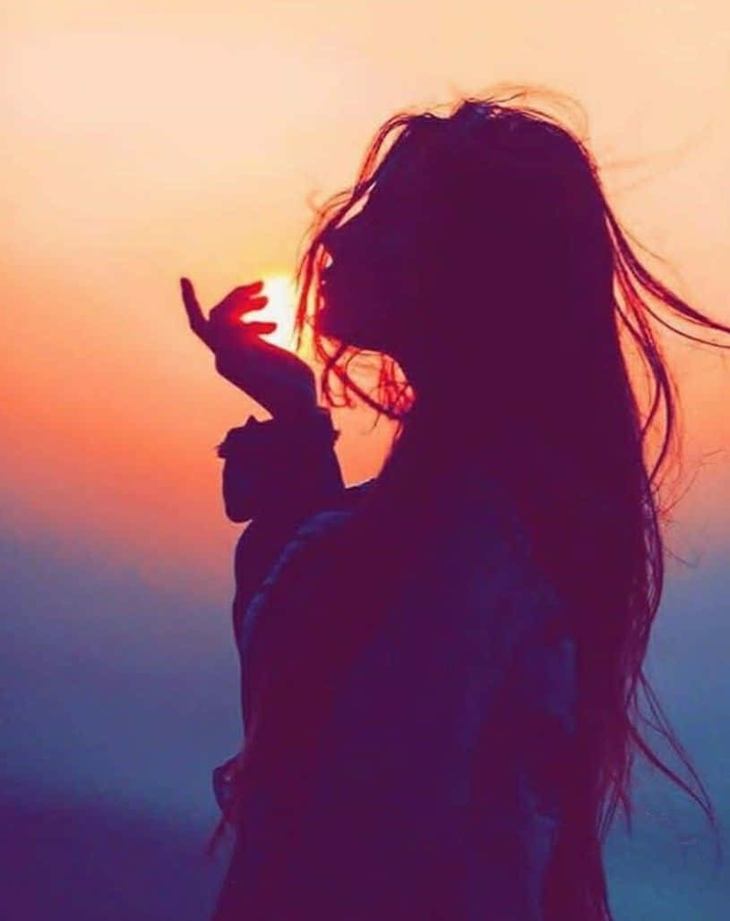 剪影中的女性，頭髮被風吹動，伸向日落。