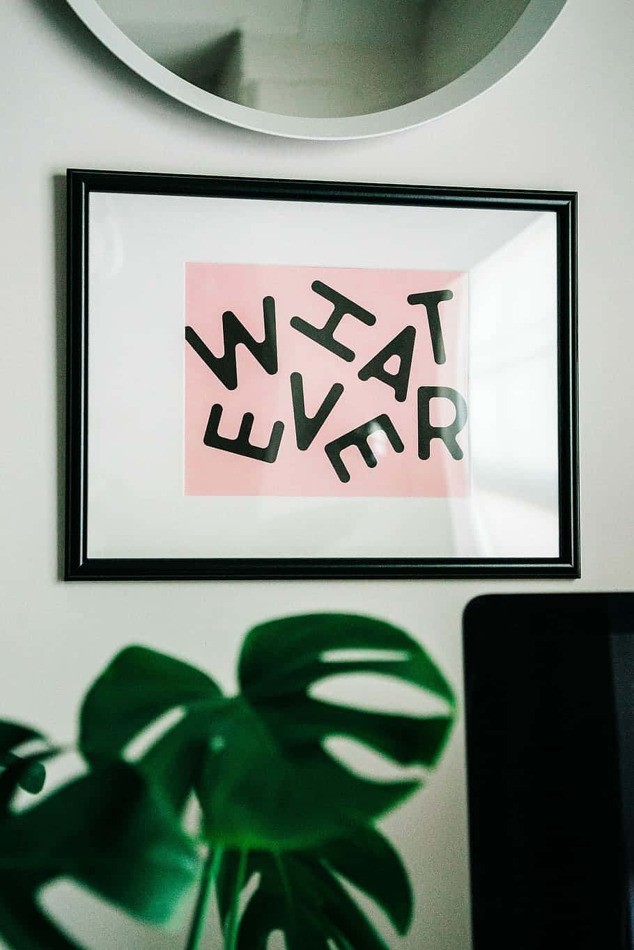 裱框粉紅色 'WHAT EVER' 藝術印刷品喺龜背竹葉同圓鏡上面。