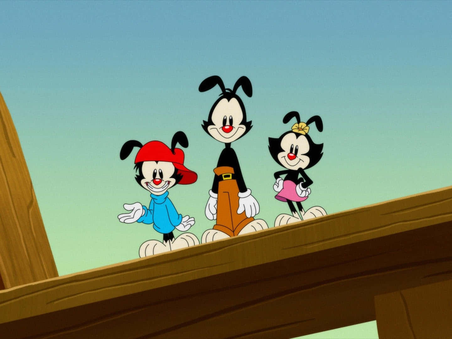 放大欣賞 Animaniacs 壁紙 — 三個經典卡通角色愉快地站在木樑上，背景是晴朗的天空。