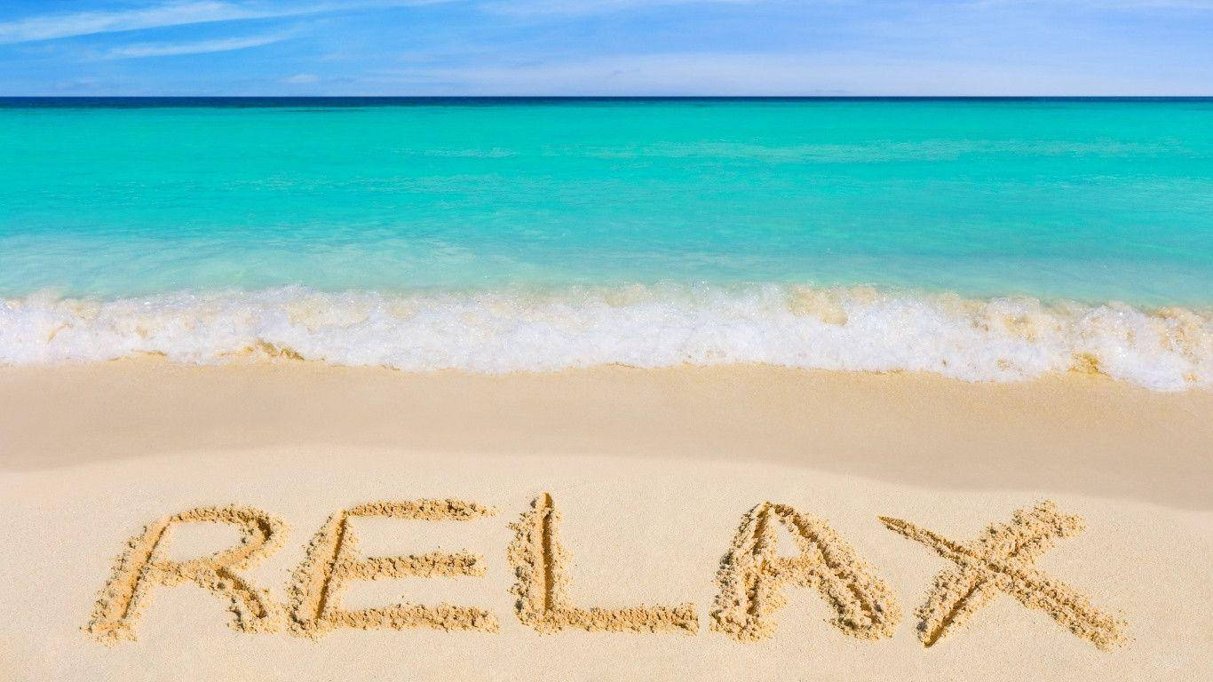 放鬆海灘訊息 壁紙 — 「relax」這個字寫在純淨沙灘的沙子上，碧綠色的海浪在清澈藍天下輕輕翻滾。