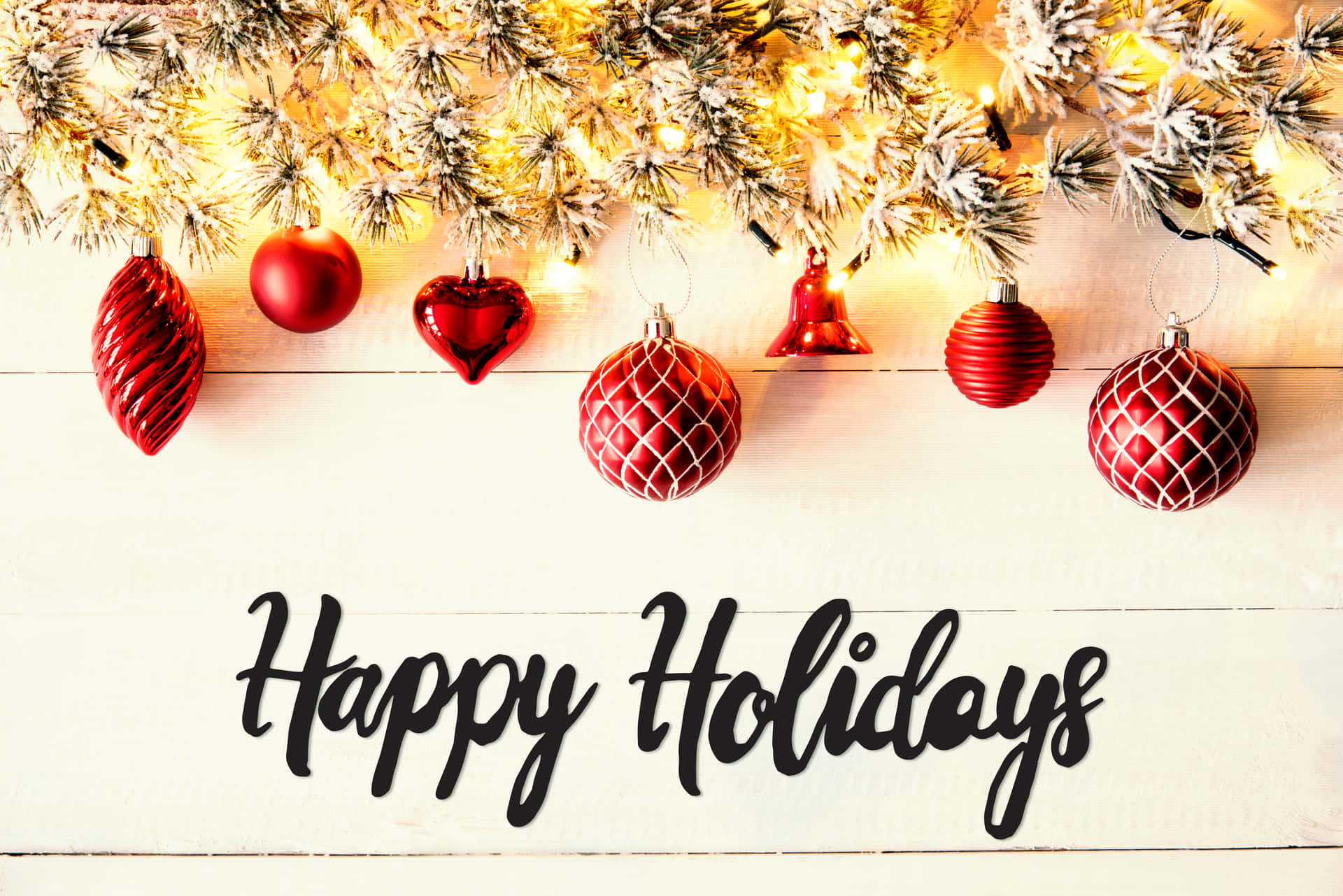 白色木頭上的「Happy Holidays」文字與紅色裝飾品和雪松枝。