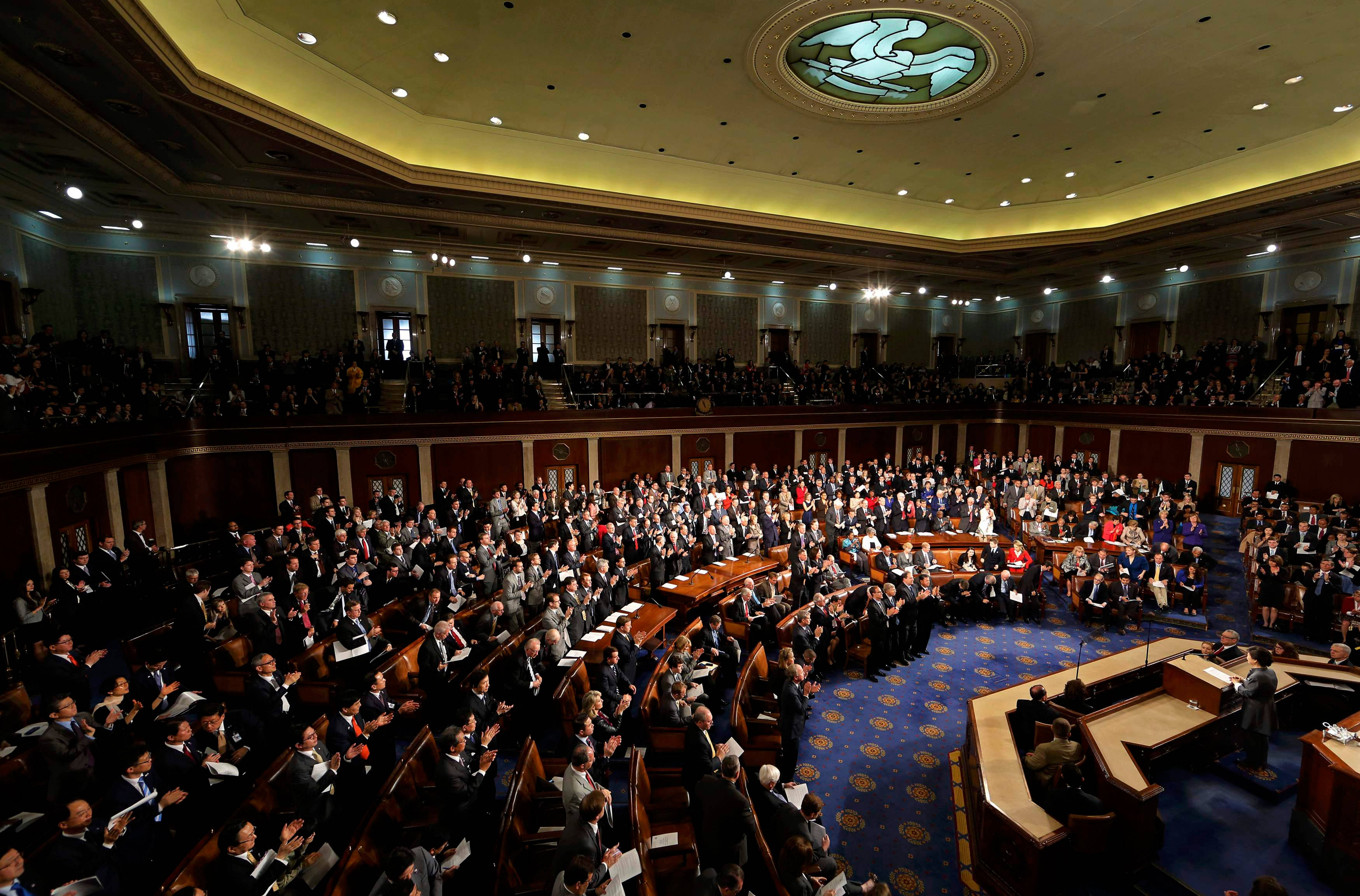 政治參議員群聚討論 壁紙 — 一個宏偉的立法會議廳，充滿了穿著正式服裝的立法者在溫暖的金色燈光和彩色玻璃穹頂下鼓掌。