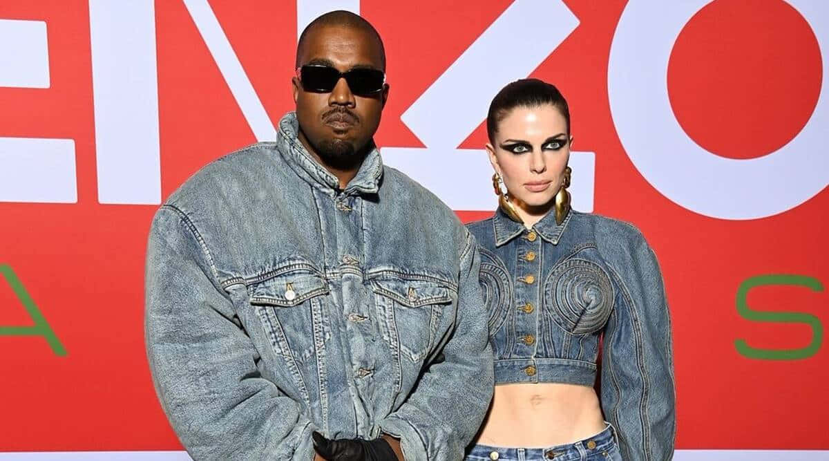 「效法內在茱莉亞·福克斯——優雅、果敢、無懼」 壁紙 — Kanye West 和一位穿著牛仔服裝的女性在一個大膽的紅白品牌背景前自信地擺姿勢。
