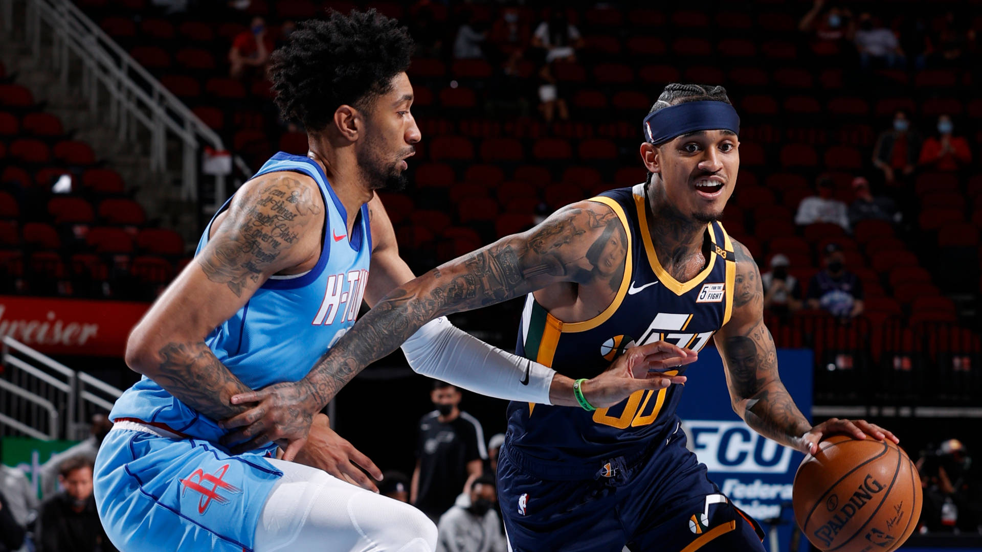 敏捷籃球員Jordan Clarkson 壁紙 — 兩名有紋身的籃球運動員在光線明亮的場館中激烈爭奪球權。