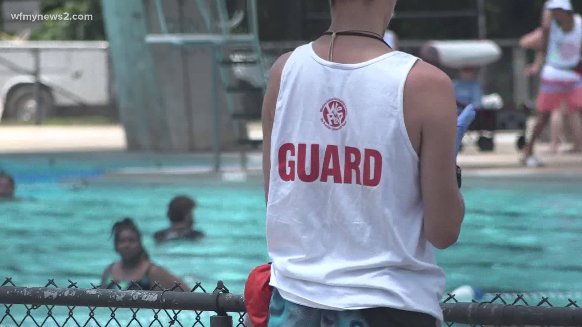 救生員在陽光明媚的日子裡觀察有圍欄的室外游泳池中的游泳者。
