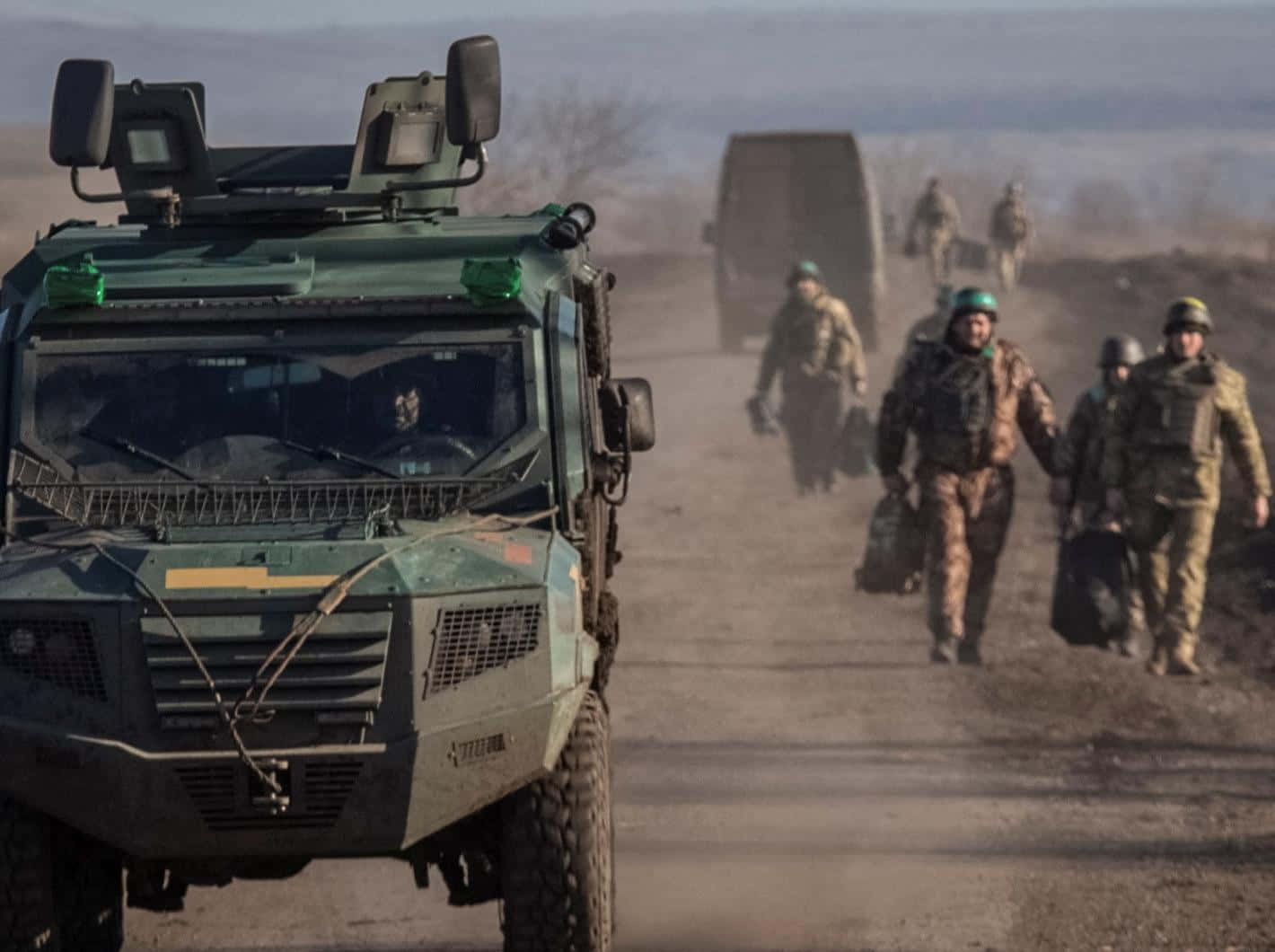 敘利亞戰火紛飛 壁紙 — 軍事車隊，裝甲車和士兵在多雲的天空下穿越塵土飛揚的地形行進。