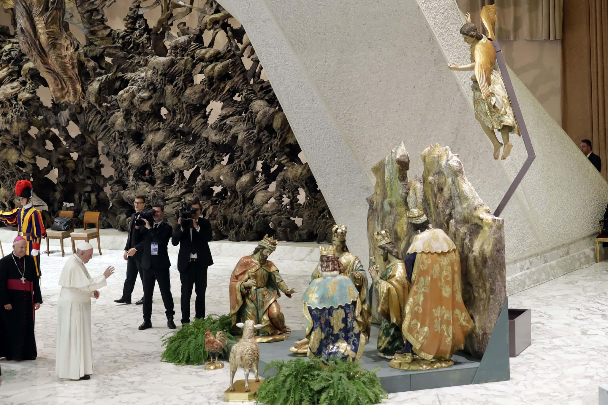 Nativity Scene 桌布 壁紙 — 教宗方濟各在一個巨大的紋理牆壁雕塑的大理石大廳中，在裝飾華麗的三王金色雕像旁做手勢。