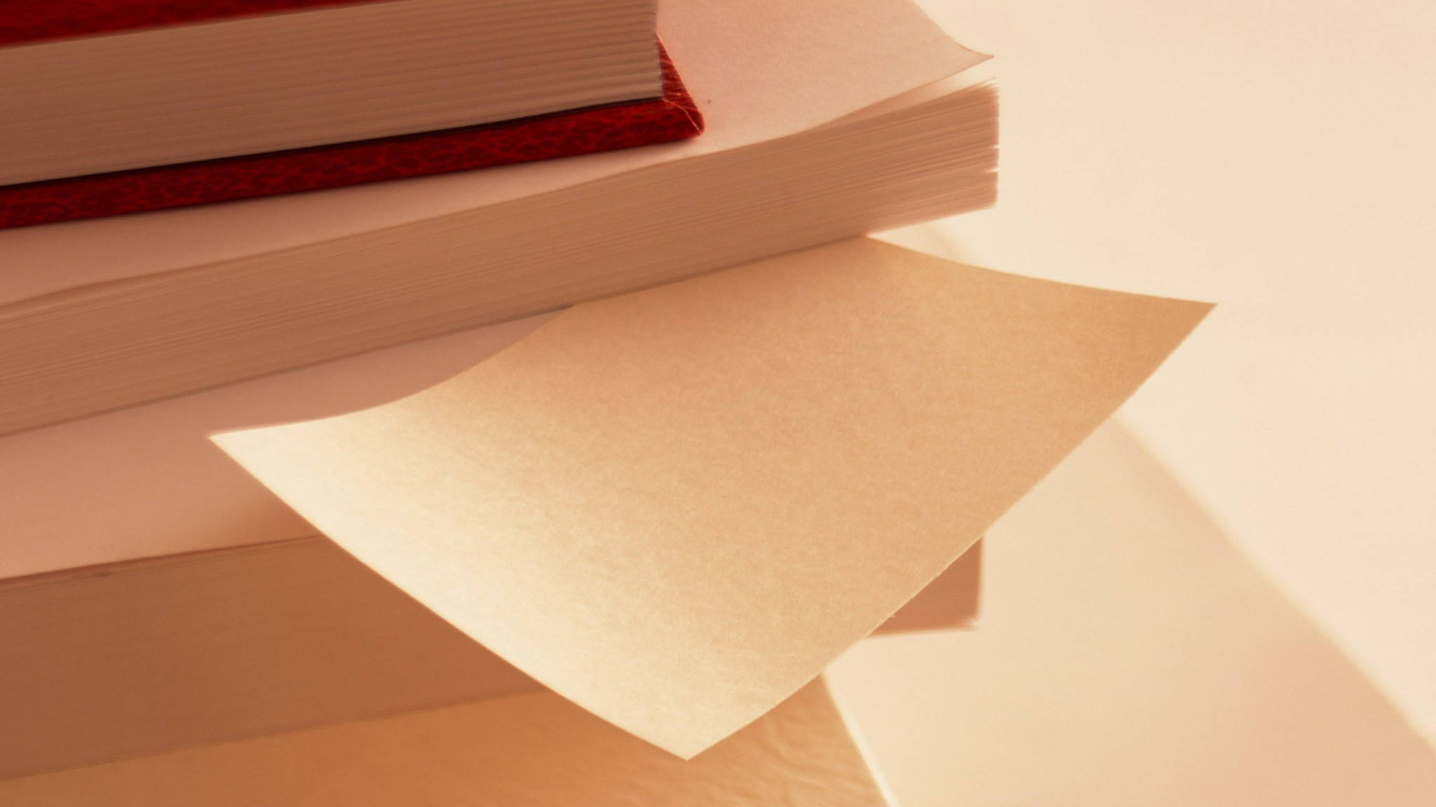 教育紙張 壁紙 — 一堆書，單張紙在溫暖的金色燈光下呈扇形展開。