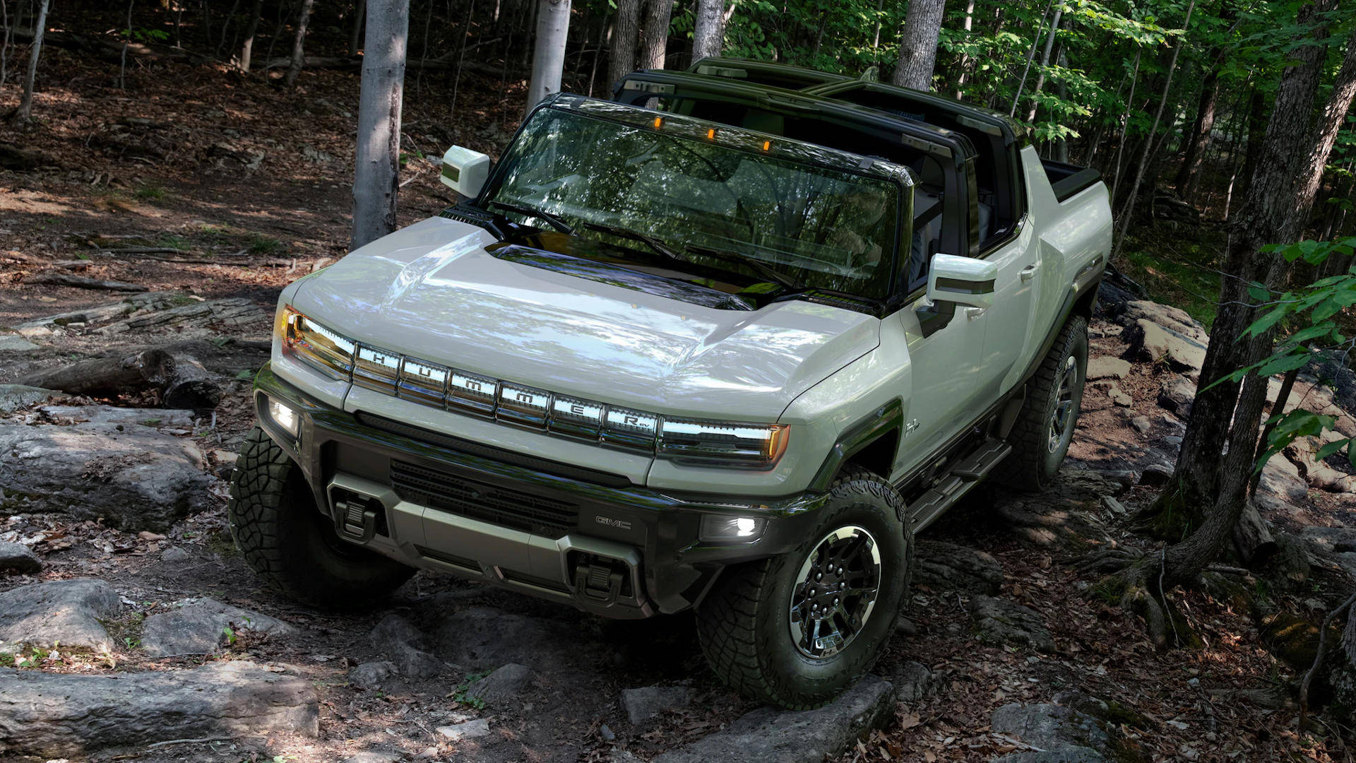 淺綠色Hummer EV pickup truck在岩石森林小徑上行駛。