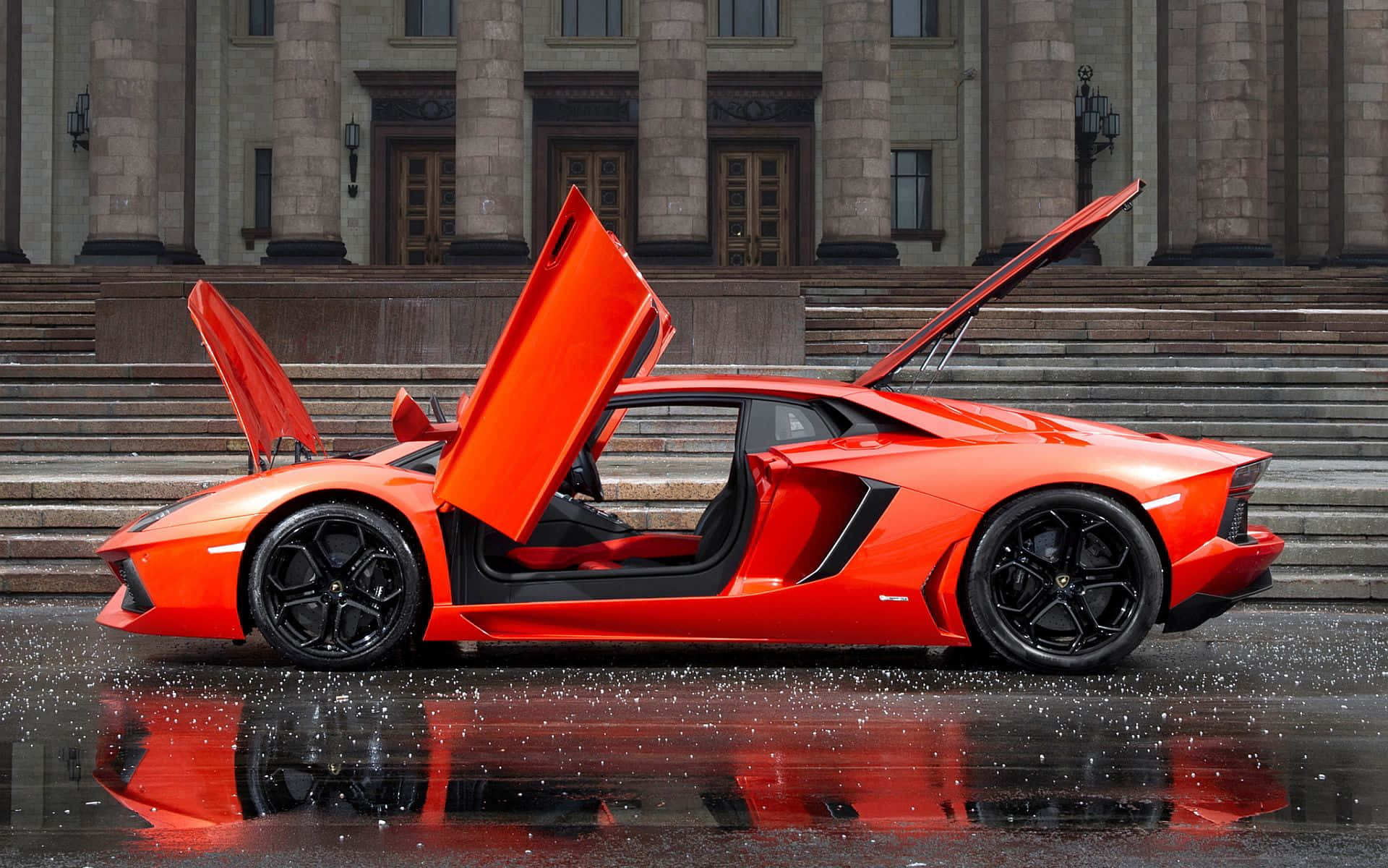 橙色林寶堅尼Aventador在石建築前的潮濕路面上打開車門。