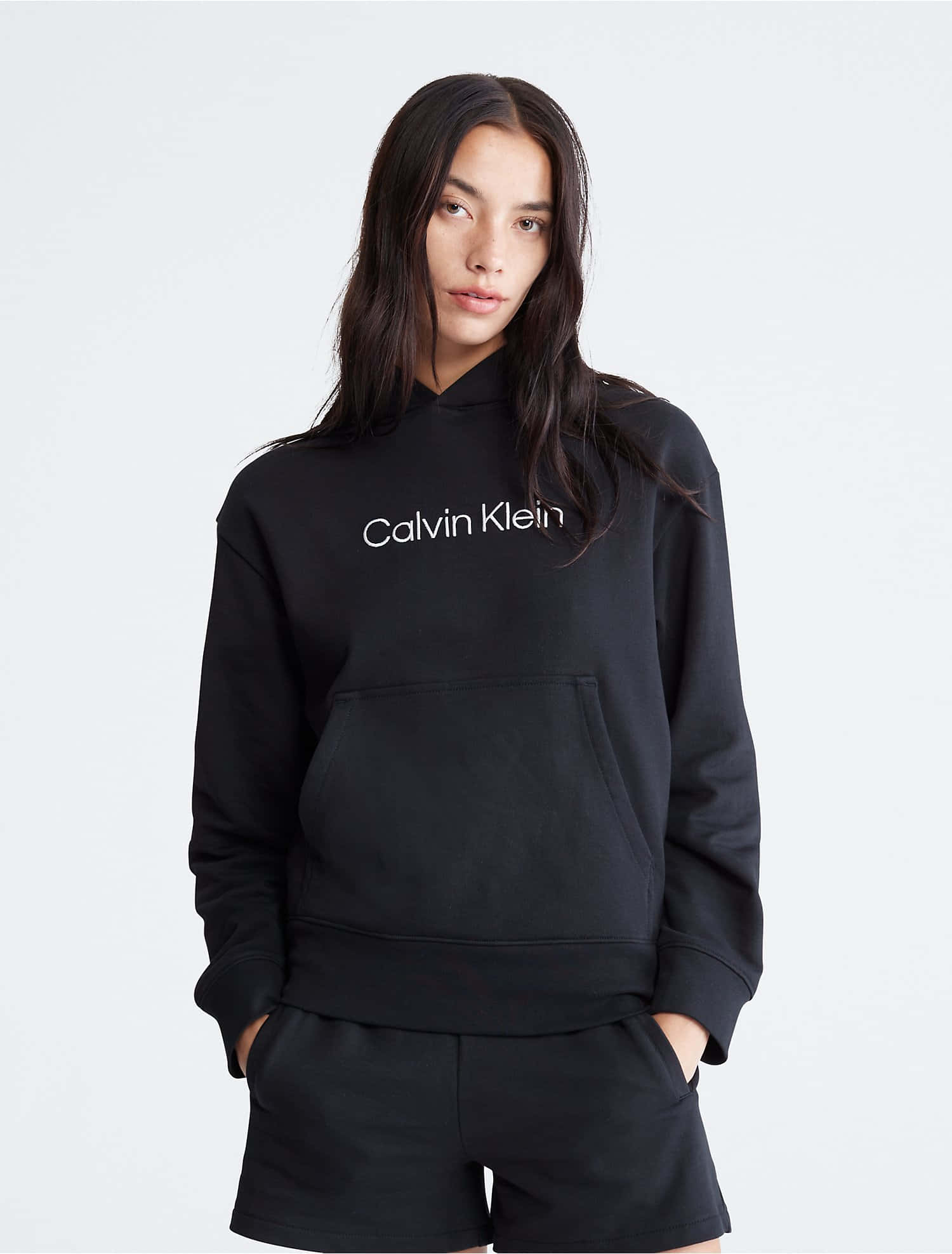 敢於表達，自信無畏 壁紙 — 一名身穿黑色Calvin Klein連帽衛衣和短褲的女性，雙手插袋，站在純白色背景前。