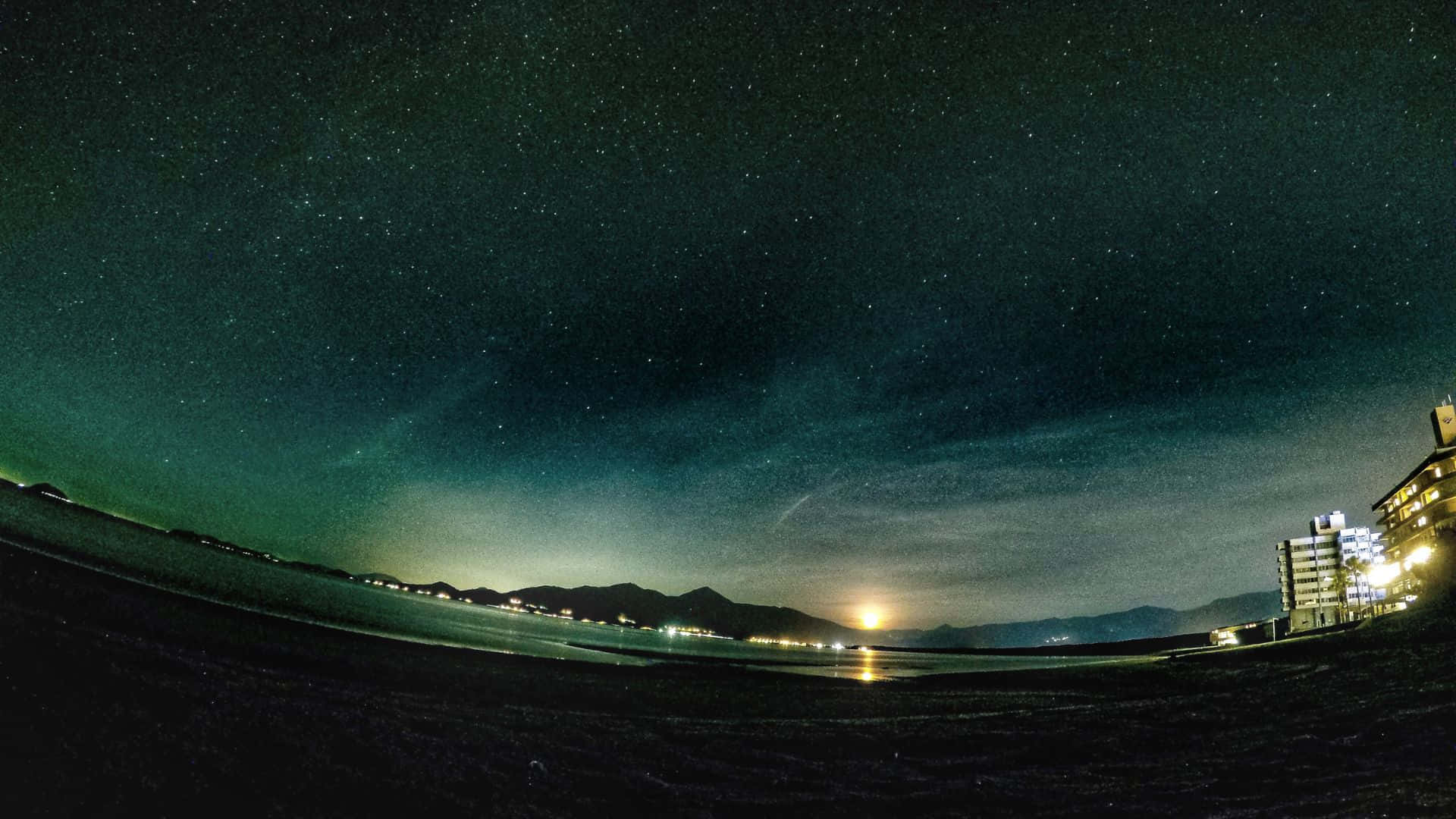 海灘上的星空之夜，城市燈光和山脈