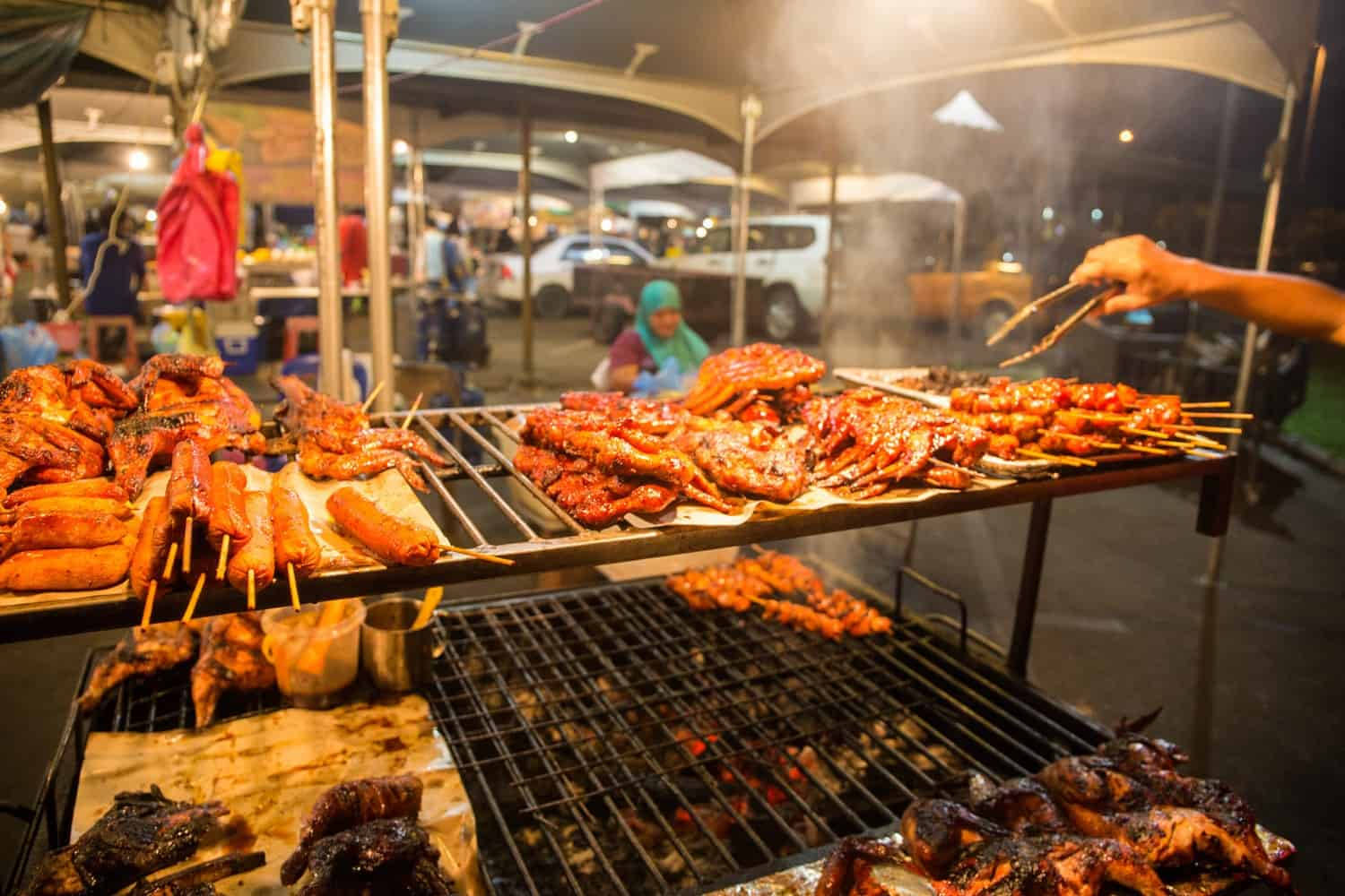 文萊街頭美食 壁紙 — 熱鬧嘅夜市燒烤爐上，喺溫暖燈光下，串住發光嘅肉同香腸嘅串燒滋滋作響。