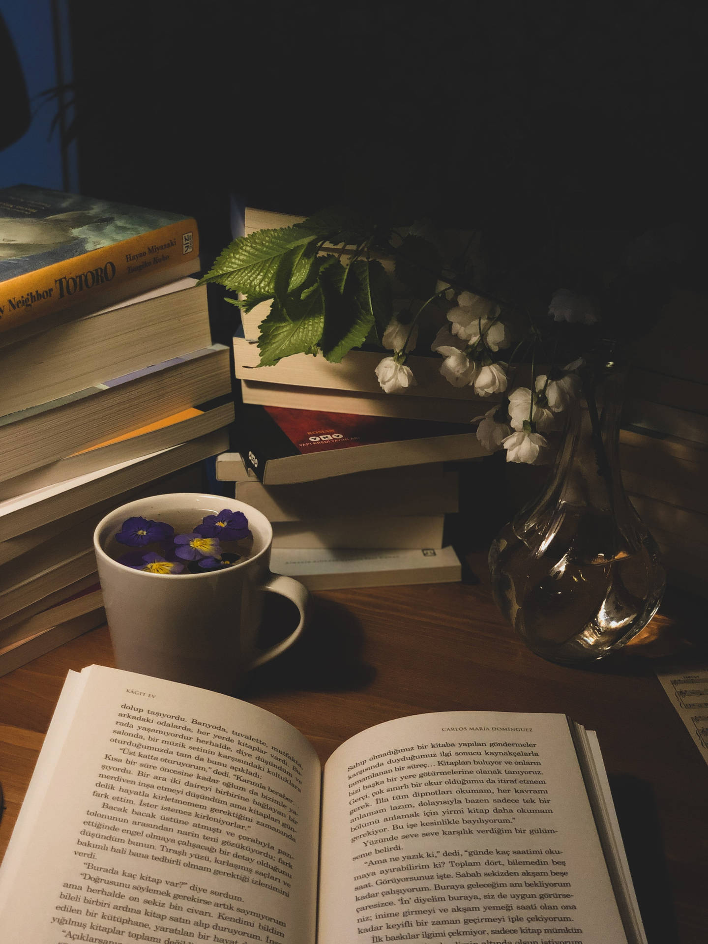 舒適的閱讀設置，有打開的書、花杯和木桌上的書。
