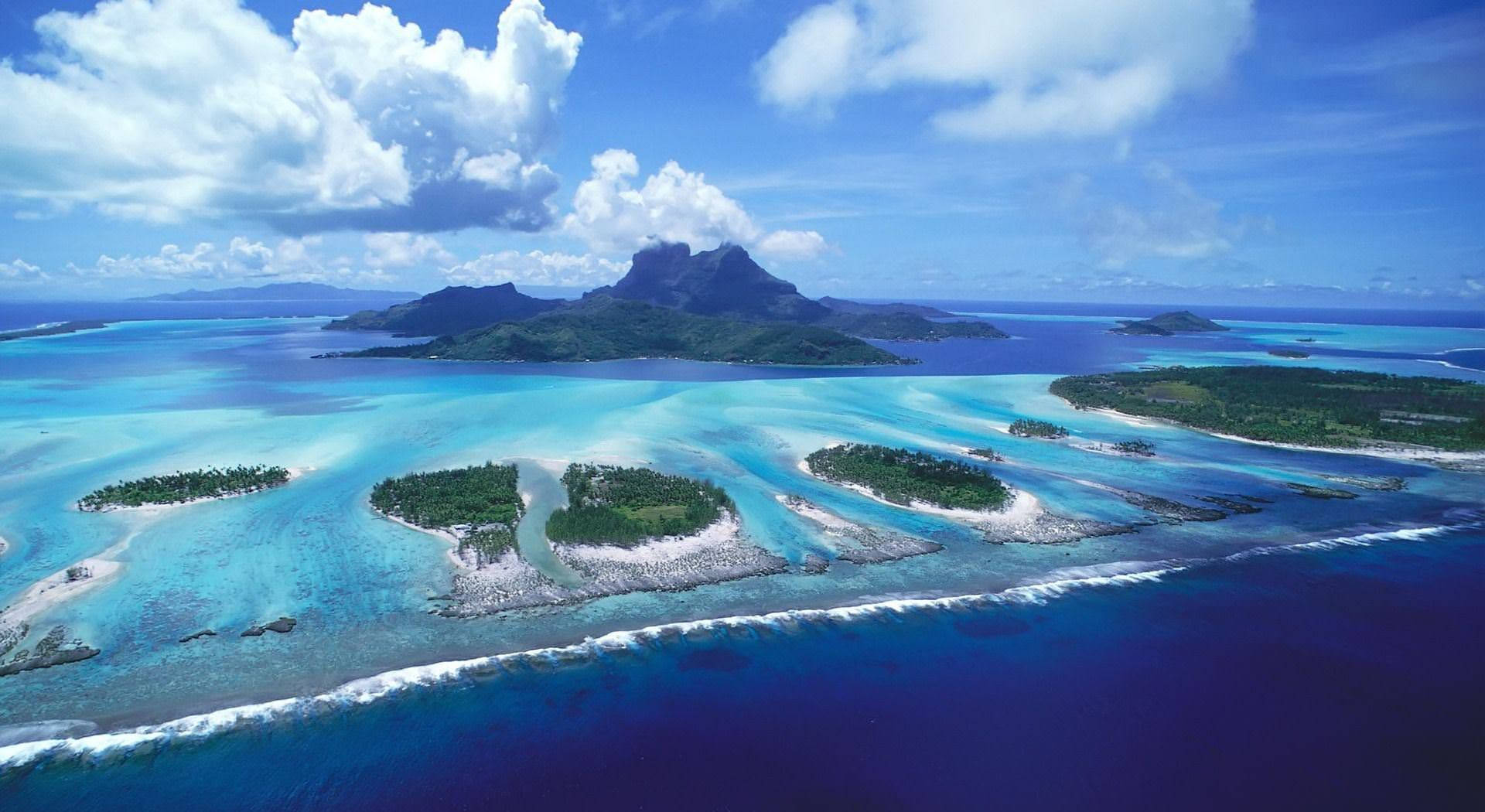 熱帶環礁，有碧綠的潟湖、珊瑚礁和鬱鬱蔥蔥的綠色島嶼，在明亮的藍天下。